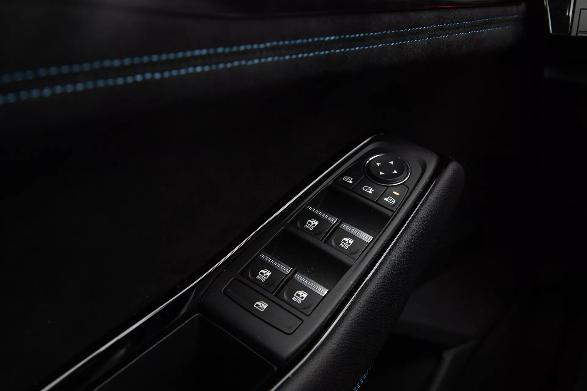 Primo piano dei comandi porta lato conducente Renault Austral 2022 con pulsanti per i finestrini elettrici con funzione a un tocco, manopola per regolazioni specchietti laterali elettronici e interruttore di blocco centrale, incastonati in un pannello nero con bordo cromato e cuciture accentate in blu sul bracciolo.