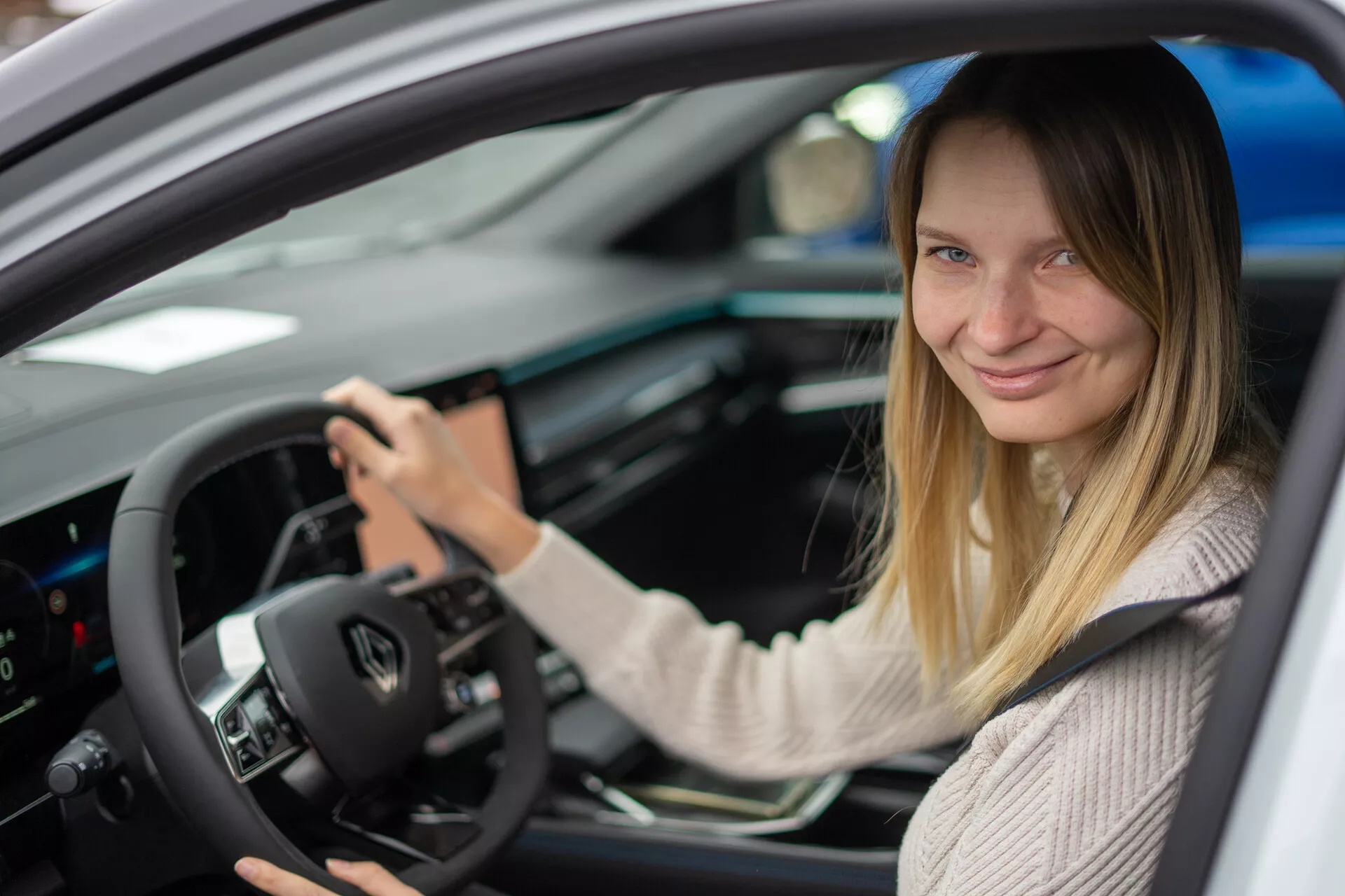 Vista interna del Renault Austral 2022 focalizzata sul lato del conducente con una donna al sedile di guida, presentando comandi montati sul volante, cruscotto digitale e console centrale con interfaccia touchscreen.