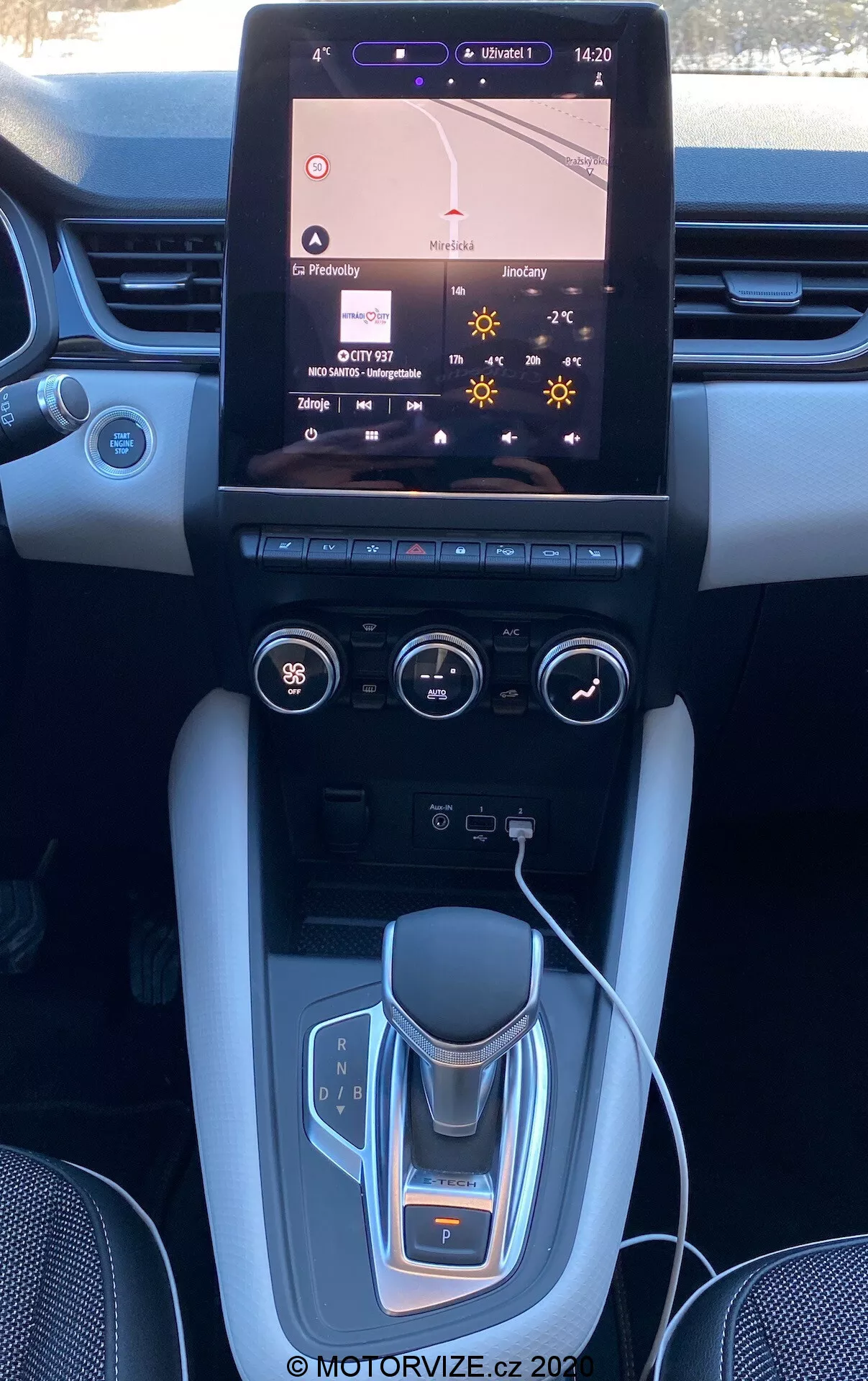Interni della Renault Captur 2020 che mostrano la console centrale e il cruscotto con un grande sistema di infotainment touchscreen che mostra la mappa di navigazione, controlli del clima a doppia zona, selettore del cambio elettronico, portabicchieri, accenti in metallo spazzolato e possibili finiture di lusso.