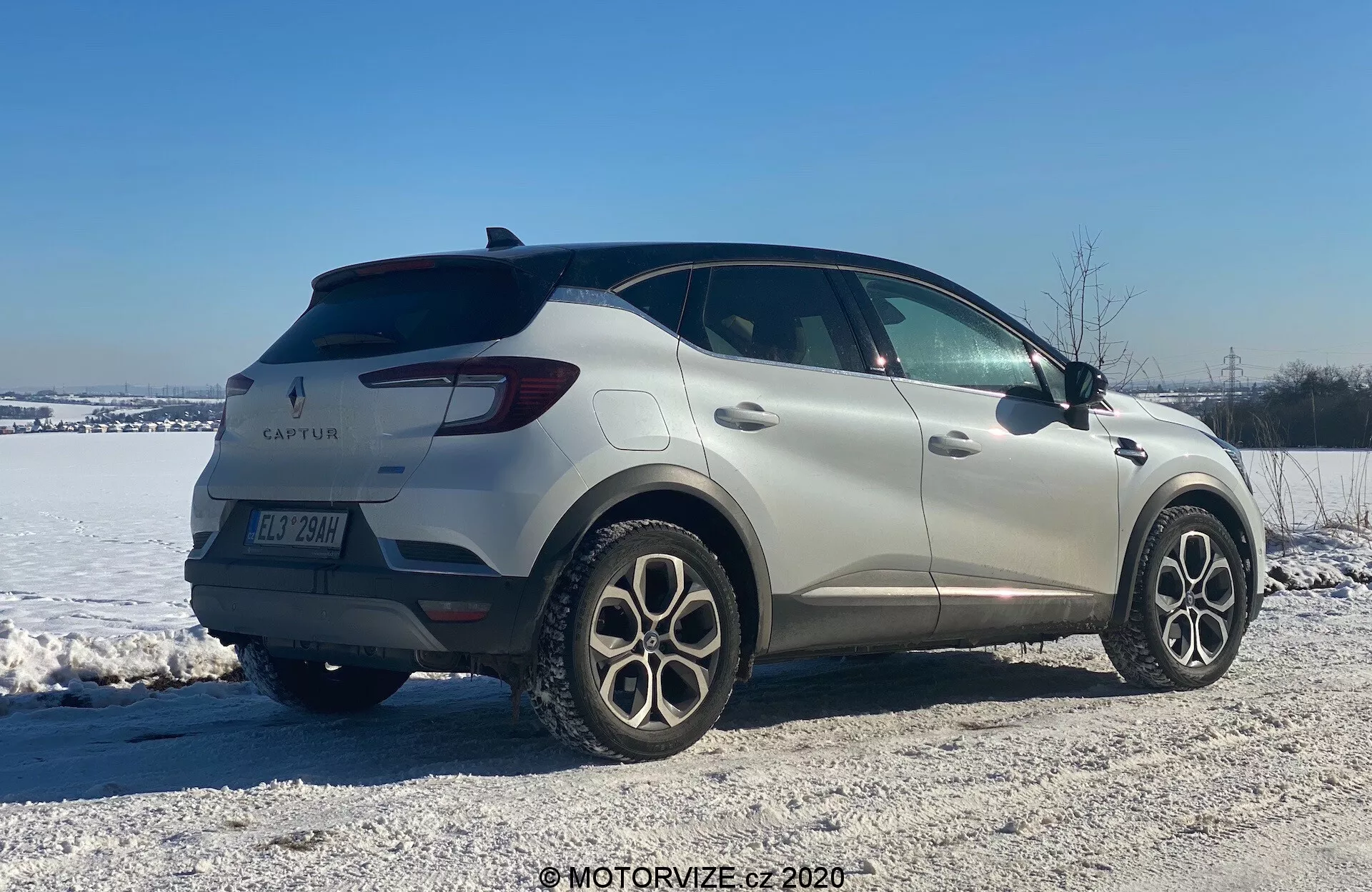 Immagine di una Renault Captur 2020, un SUV compatto, in un ambiente invernale. Mostrato da una vista posteriore tre quarti, l'auto presenta un design elegante con linee fluide e luci posteriori a LED. Il marchio del produttore e il nome del modello sono visibili insieme a ruote in lega a più razze, sensori di parcheggio posteriori e specchietti laterali con indicatori di direzione integrati. Parcheggiato in un'area con neve e ghiaia, l'immagine suggerisce abilità su terreni variati e condizioni invernali.