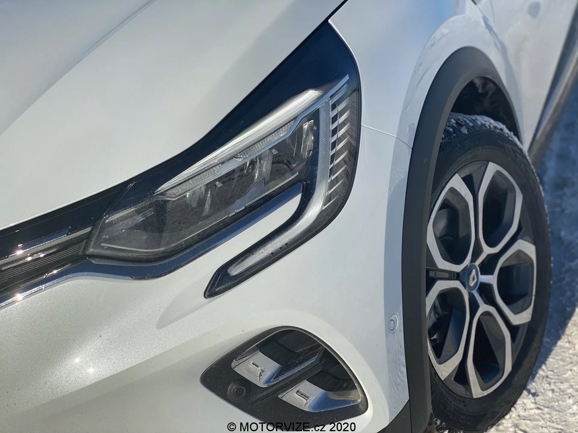 Vista ravvicinata del Renault Captur 2020 focalizzata sul quarto anteriore sinistro, che mostra fari LED eleganti, cerchi in lega multi-razza eleganti, paraurti anteriore dinamico con prese d'aria e finiture cromate lucide su una carrozzeria bianca brillante.
