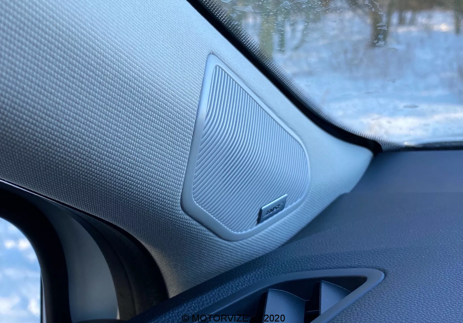 Primo piano degli interni di una Renault Captur 2020, evidenziando un altoparlante della portiera anteriore del passeggero con griglia a trama e marchio del sistema audio, circondato da materiali contrastanti, scattata dall'interno del veicolo.
