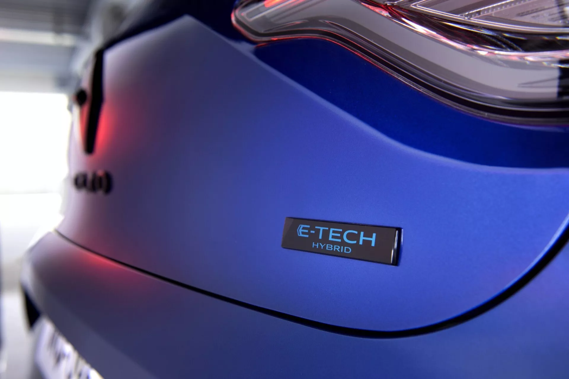 Veduta ravvicinata del Renault Clio V-Facelift 2023 con pannello posteriore, distintivo E-TECH HYBRID e vernice blu metallico