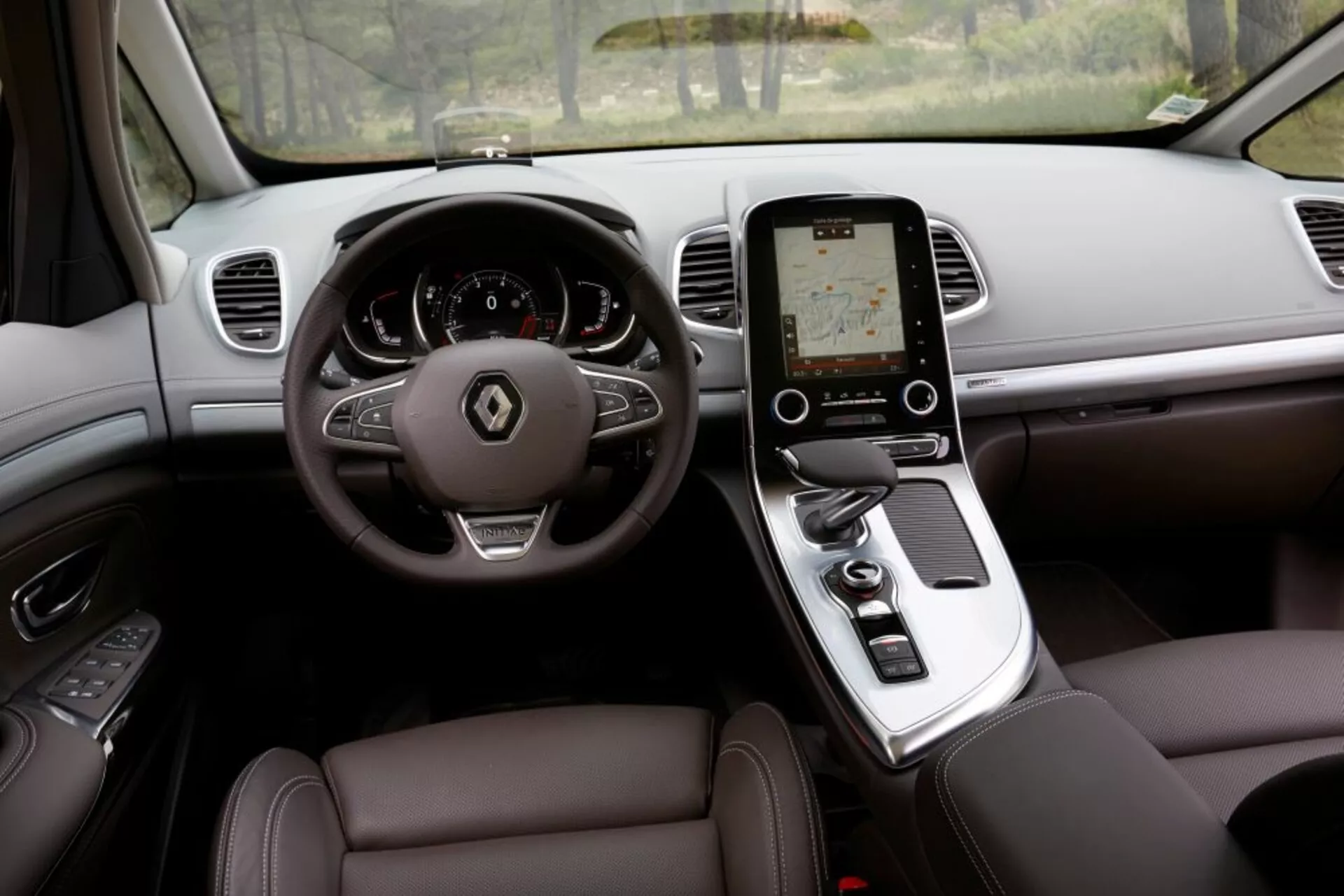 Vista interna del Renault Espace 2015 da prospettiva del conducente con caratteristiche lussuose, volante a tre razze con comandi, cruscotto digitale, console centrale con touchscreen verticale per l'infotainment, cambio automatico, sedili in pelle con regolazione elettronica, bocchette d'aria sul cruscotto per il controllo del clima