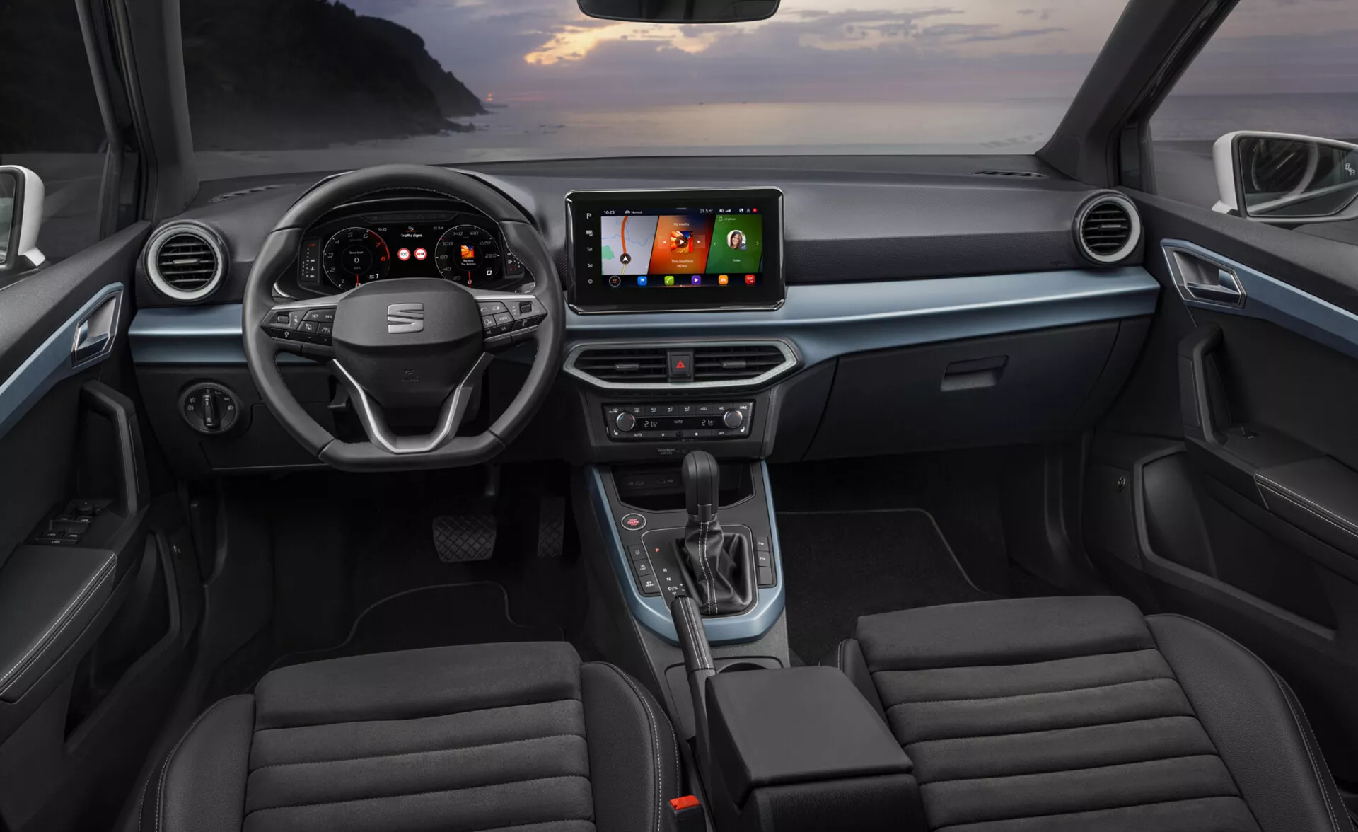 Vista interna di una Seat Arona 2017 dai sedili posteriori che mostra la plancia con volante, gruppo strumenti, console centrale, sistema di infotainment e sedili anteriori con design moderno e tecnologia avanzata come display digitali, navigazione GPS e integrazione smartphone