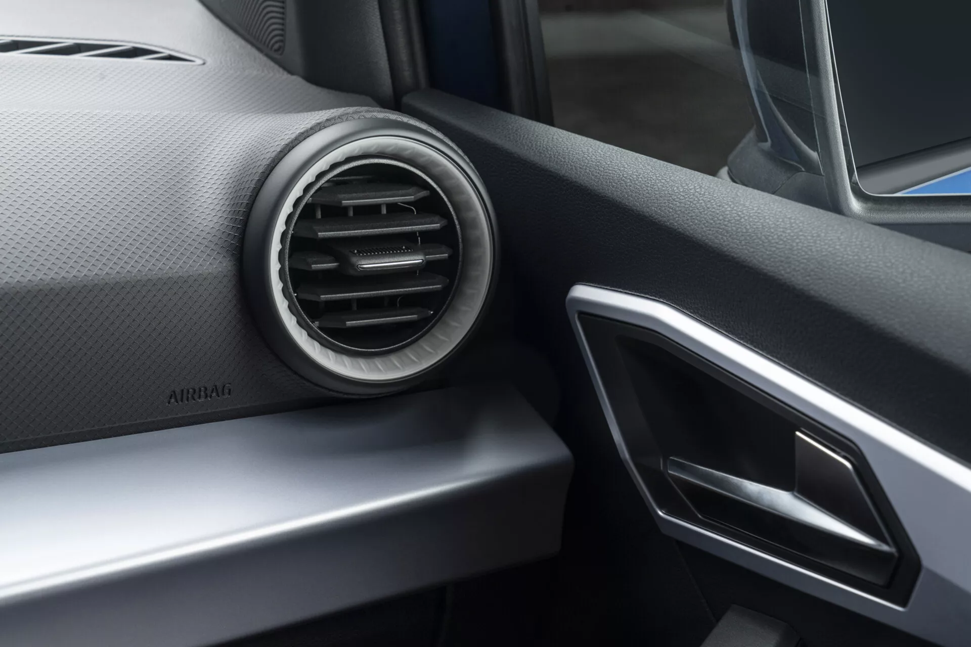 Vista interna della Seat Arona 2017 focalizzata sulla parte del cruscotto lato passeggero con bocchetta dell'aria condizionata circolare, accenti argento e anteposizione del sistema di infotainment