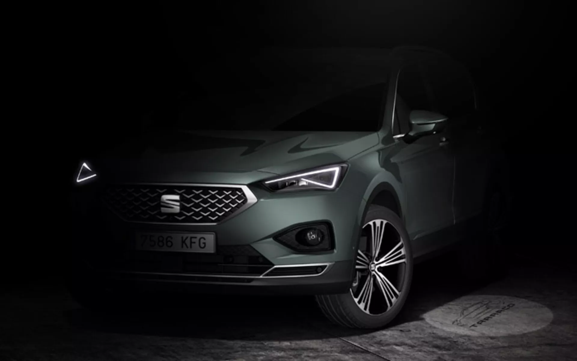 Seat Tarraco 2019 esposta in un'ambientazione scura e malinconica che enfatizza il suo frontale elegante, griglia geometrica, fari LED con distintive luci diurne e cofano scolpito, insieme a una vista dettagliata della ruota in lega, evidenziando gli attributi di lusso e tecnologia moderna dell'auto