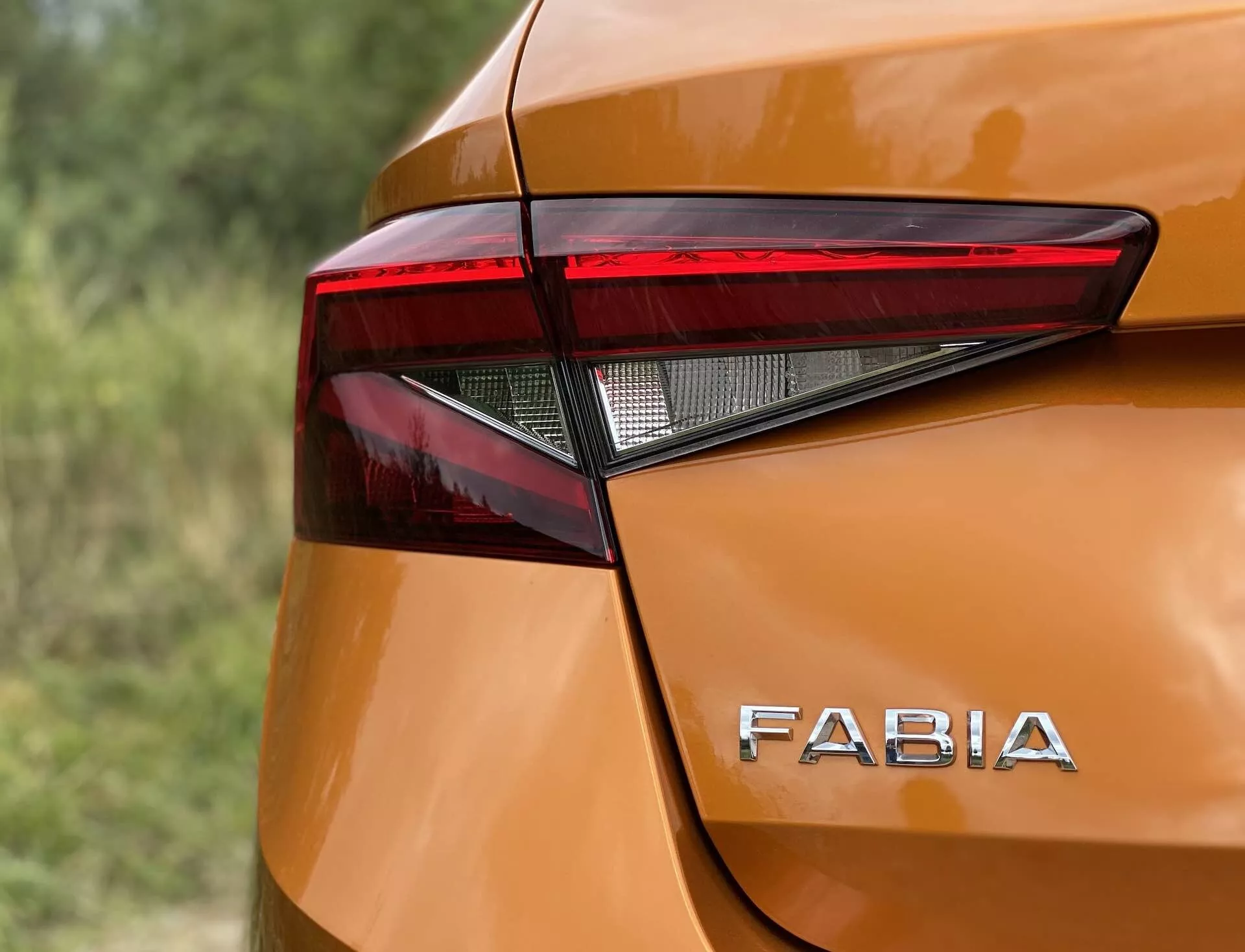 Immagine ravvicinata dell'angolo posteriore di una Skoda Fabia 2021 che mette in risalto il design angolare e affilato dell'assemblaggio delle luci posteriori a LED e l'inconfondibile marchio 'FABIA' sulla carrozzeria arancione metallizzato lucido. Le curve morbide e le leggere sporgenze intorno alle luci posteriori contribuiscono all'estetica moderna, catturata da un angolo leggermente elevato con una profondità di campo ridotta.