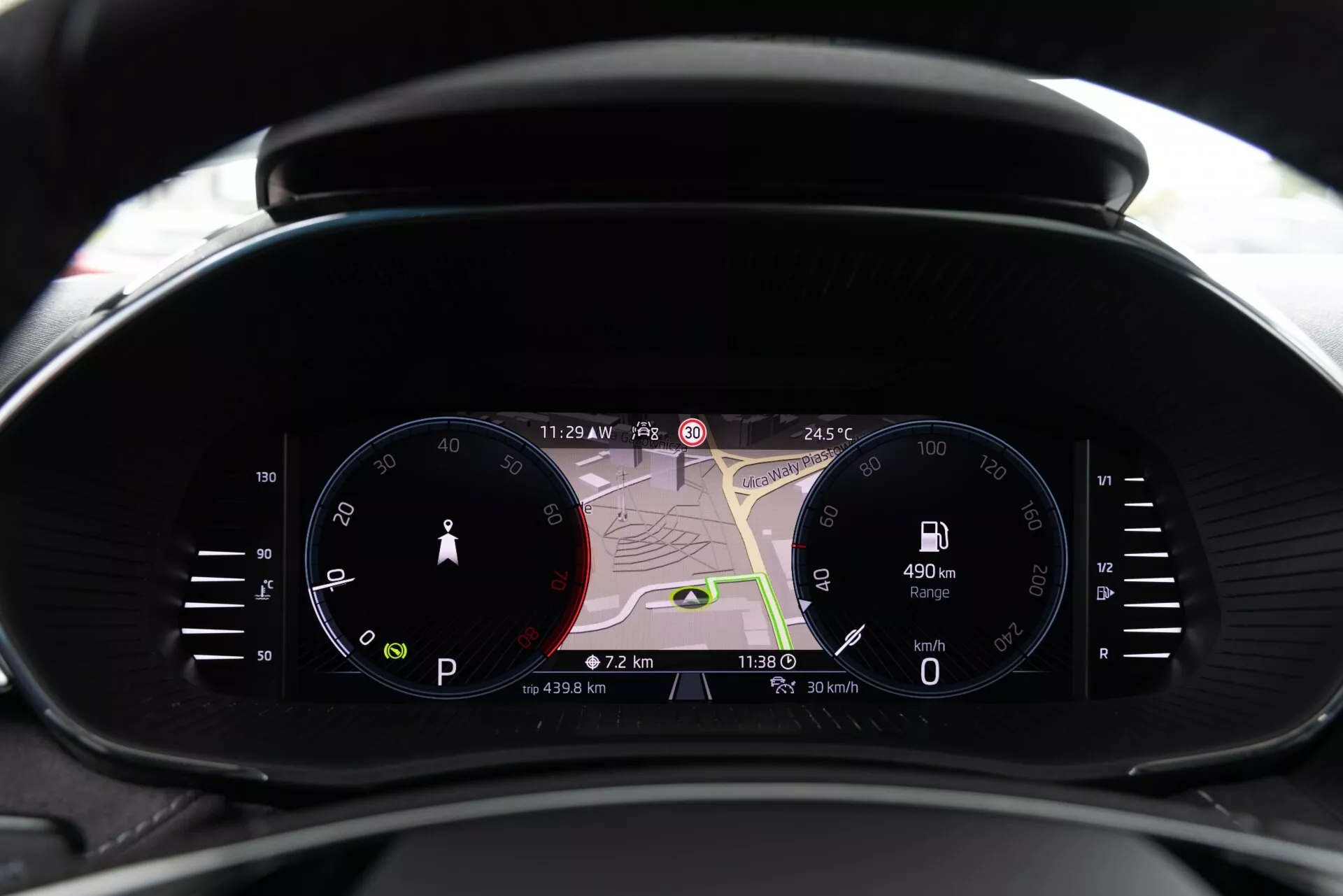 Vista ravvicinata del quadro strumenti moderno della Skoda Fabia 2021 dalla prospettiva del conducente, con un tachimetro analogico, un ampio display digitale con mappa di navigazione e un contagiri digitale. I display mostrano le 11:29 PM, 24,5°C, un'autonomia di 490 km, la velocità attuale di 0 km/h e i dati del viaggio. Combina design tradizionale e contemporaneo con tecnologia avanzata, inclusa la navigazione in tempo reale, l'informazione per il conducente e gli indicatori di connettività.