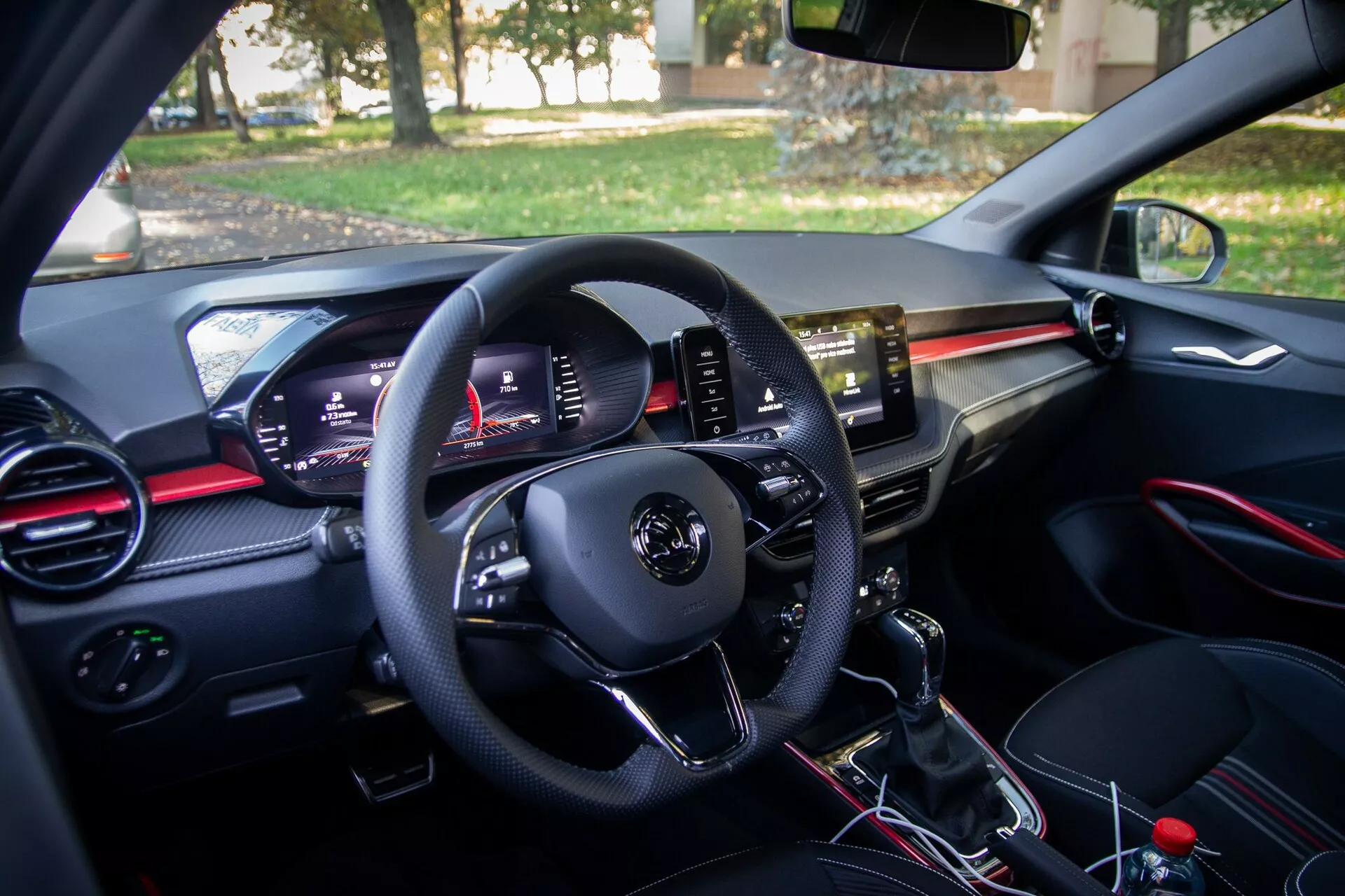 Vista dell'interno di una moderna Skoda Fabia 2021 dalla prospettiva del guidatore, con pannello di controllo sulla portiera del guidatore, volante multifunzionale, quadro strumenti digitale, prese d'aria con accenti rossi, touchscreen di infotainment centrale, leva del cambio manuale e area del sedile passeggero con vano portaoggetti e presa d'aria abbinata.