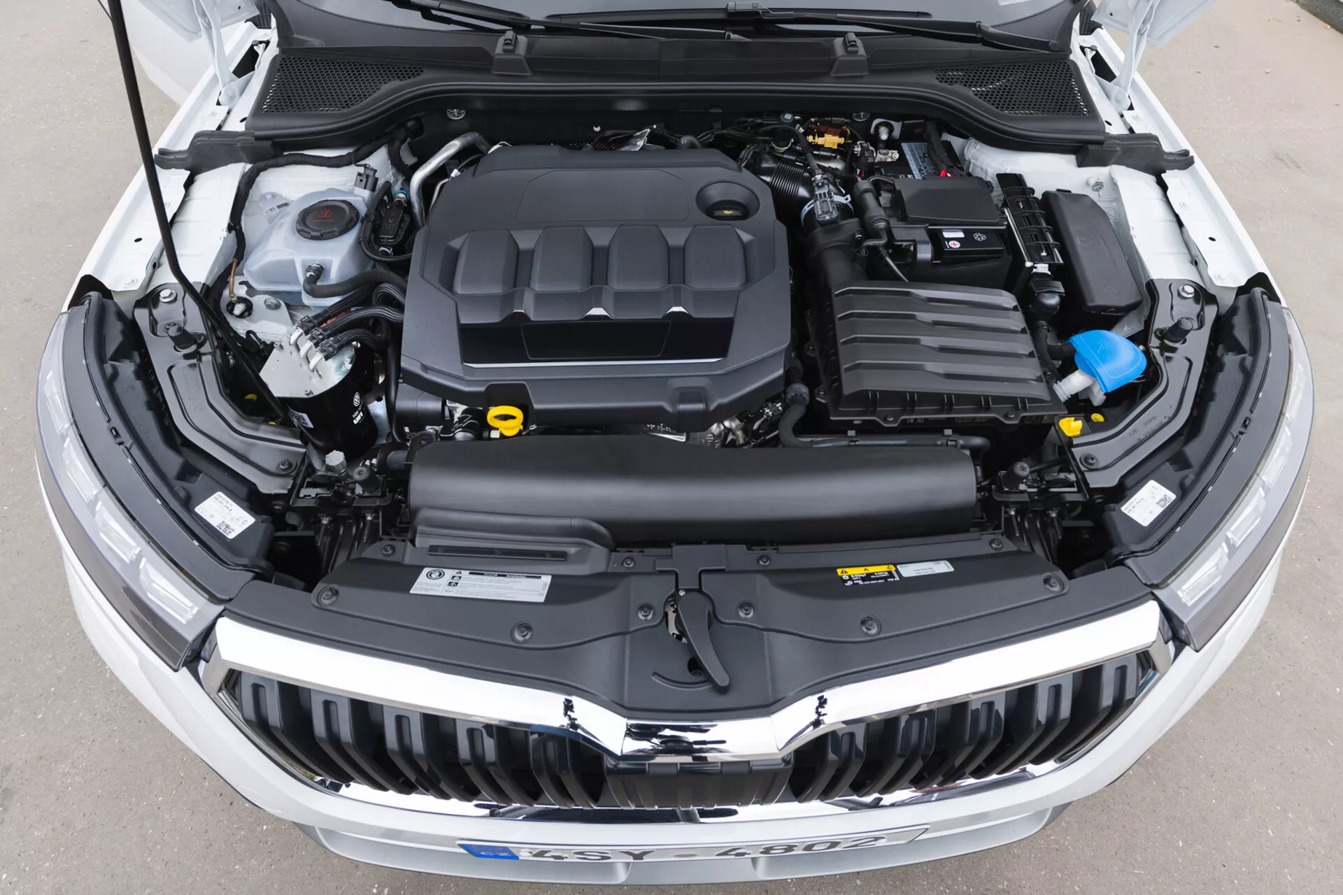 Vista ravvicinata del vano motore aperto della Skoda Kamiq 2019 che mostra il coperchio del motore, le coperture in plastica, i serbatoi dei fluidi e i condotti elettronici senza elementi di design esterno visibili