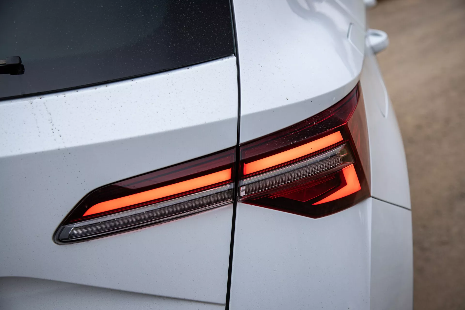 Primo piano della sezione posteriore della Skoda Karoq 2021 che mostra il design moderno della luce posteriore LED, con un'enfasi sulle linee angolari e sulla carrozzeria lucida e di colore chiaro con gocce d'acqua visibili