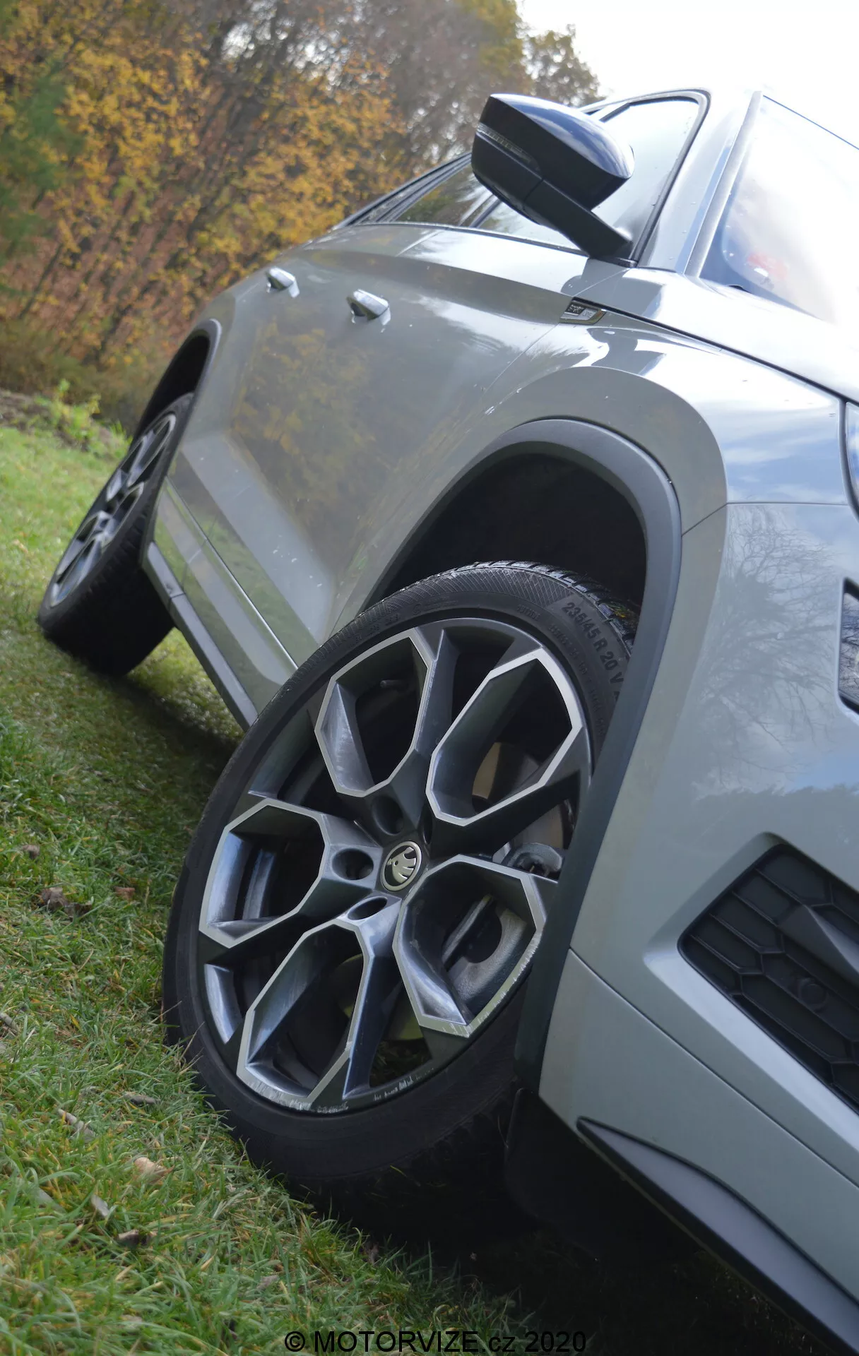 Primo piano di un SUV Skoda Kodiaq 2017, con un focus sulla ruota anteriore e sul pannello laterale inferiore. Il veicolo è mostrato da un angolo basso che ne evidenzia l'altezza e il design robusto. La ruota in lega multiraggio è leggermente girata a destra, e lo specchietto laterale con indicatore di direzione integrato è visibile. La vernice metallizzata e la superficie pulita riflettono la luce naturale, con un ambiente parco sullo sfondo.