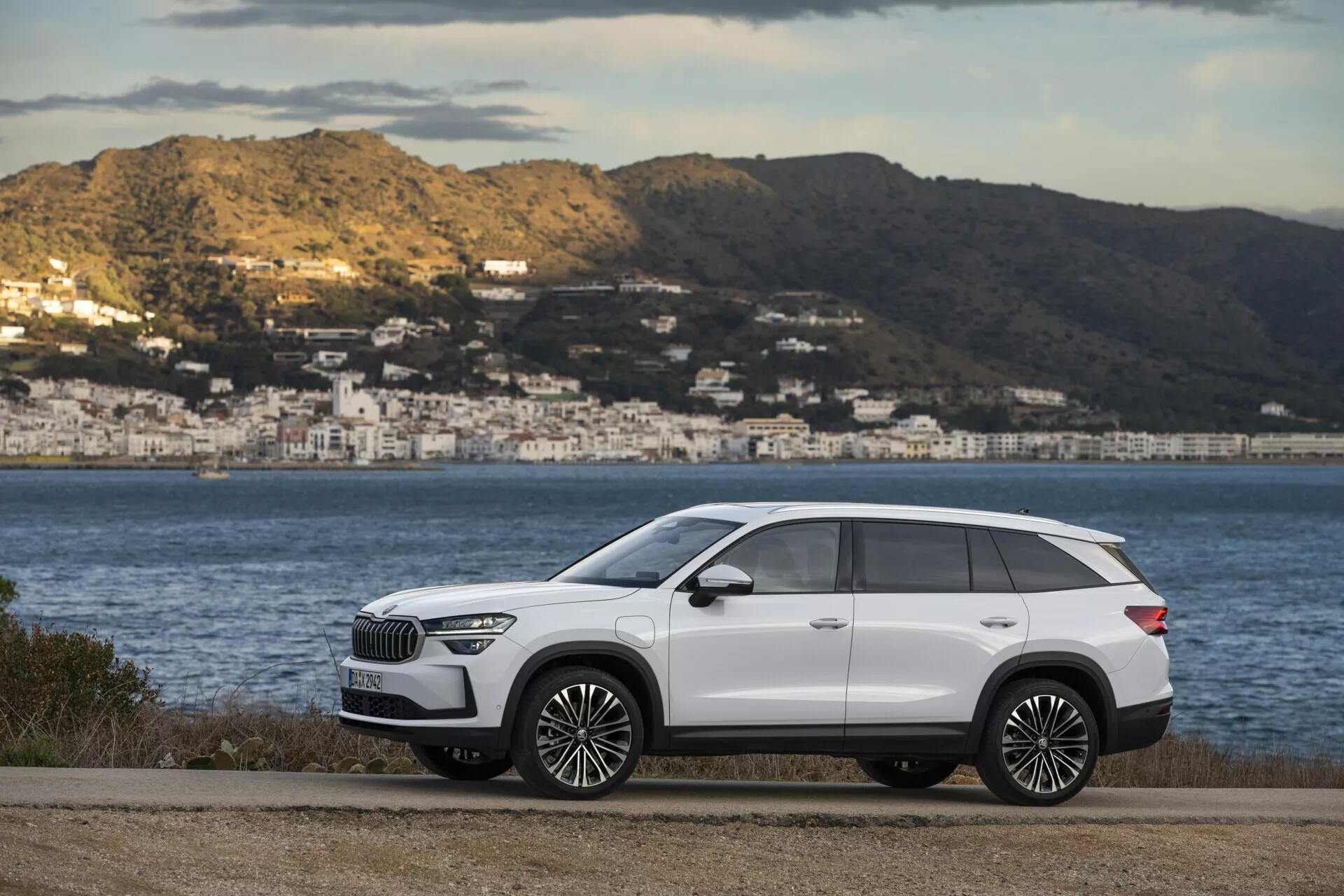 SUV premium Skoda Kodiaq bianca 2024 parcheggiata su una strada pianeggiante con scenario costiero sullo sfondo, mostra il profilo laterale elegante del veicolo con dettagli cromati e grandi cerchi in lega