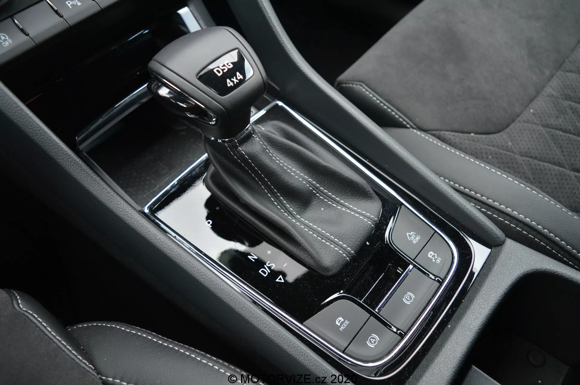 Vista ravvicinata della leva del cambio automatico e della console centrale nera lucida della Skoda Kodiaq 2017, con modalità di guida, freno di stazionamento elettronico e pulsante auto-hold; evidenzia le cuciture in pelle sulla leva con modalità sportiva.