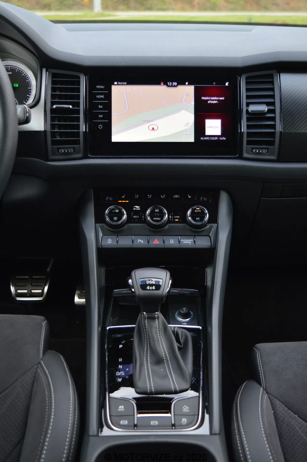 Vista interiore di una Skoda Kodiaq 2017 che mostra la console centrale, il sistema di infotainment touchscreen che mostro una mappa, manopole di controllo del clima duali, leva del cambio, selettore della modalità di guida, portabicchieri, sedili in pelle con cuciture a contrasto e pulsante di avviamento senza chiave
