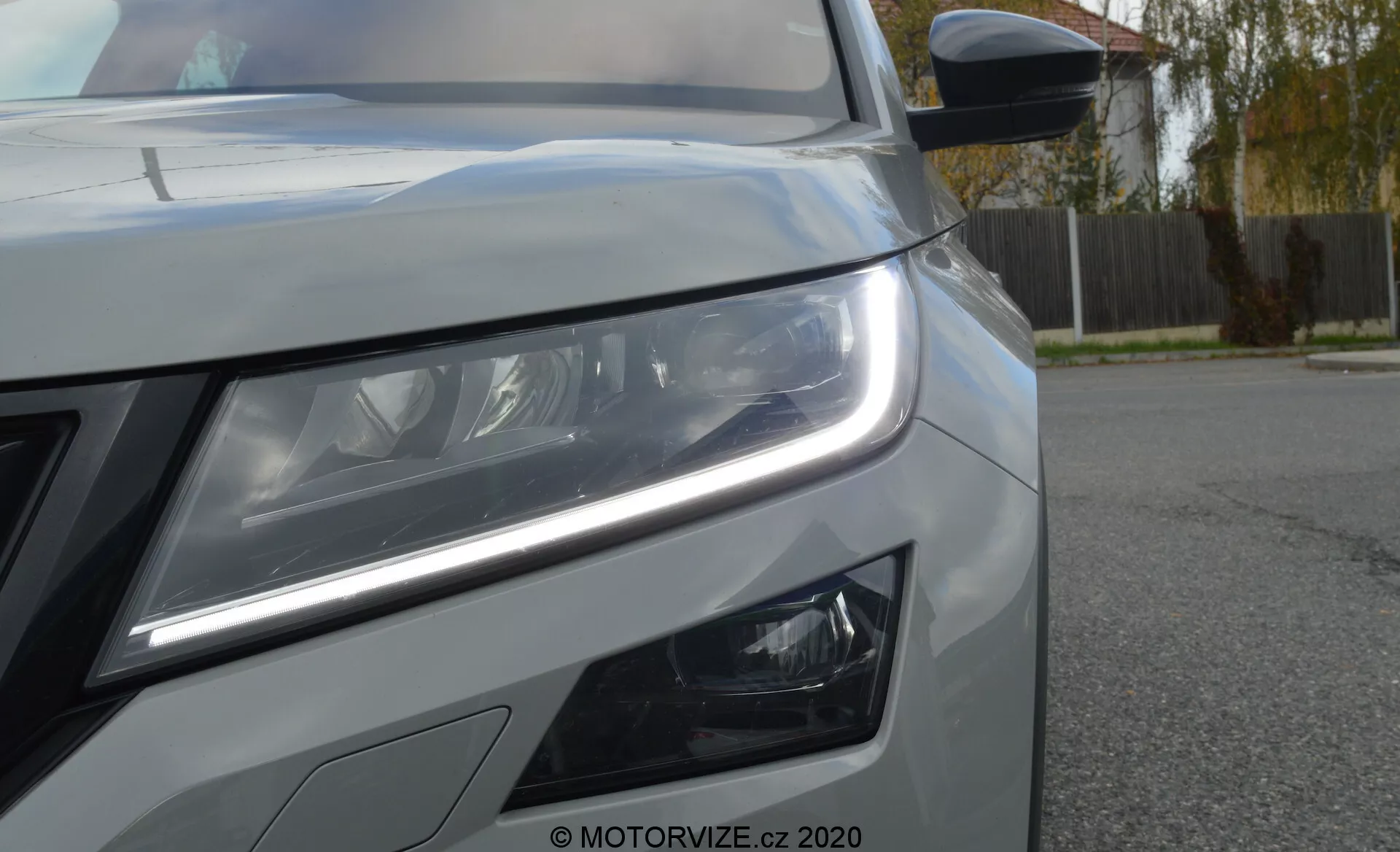 Primo piano della parte anteriore sinistra della Skoda Kodiaq 2017, che mostra l'avanzato gruppo ottico a LED con luci diurne e lenti a proiezione. L'angolazione evidenzia la tecnologia e le caratteristiche di design moderno, inclusi i fendinebbia aggiuntivi, una parte della griglia con finitura metallica, il cofano e uno specchietto laterale con indicatori di direzione integrati.