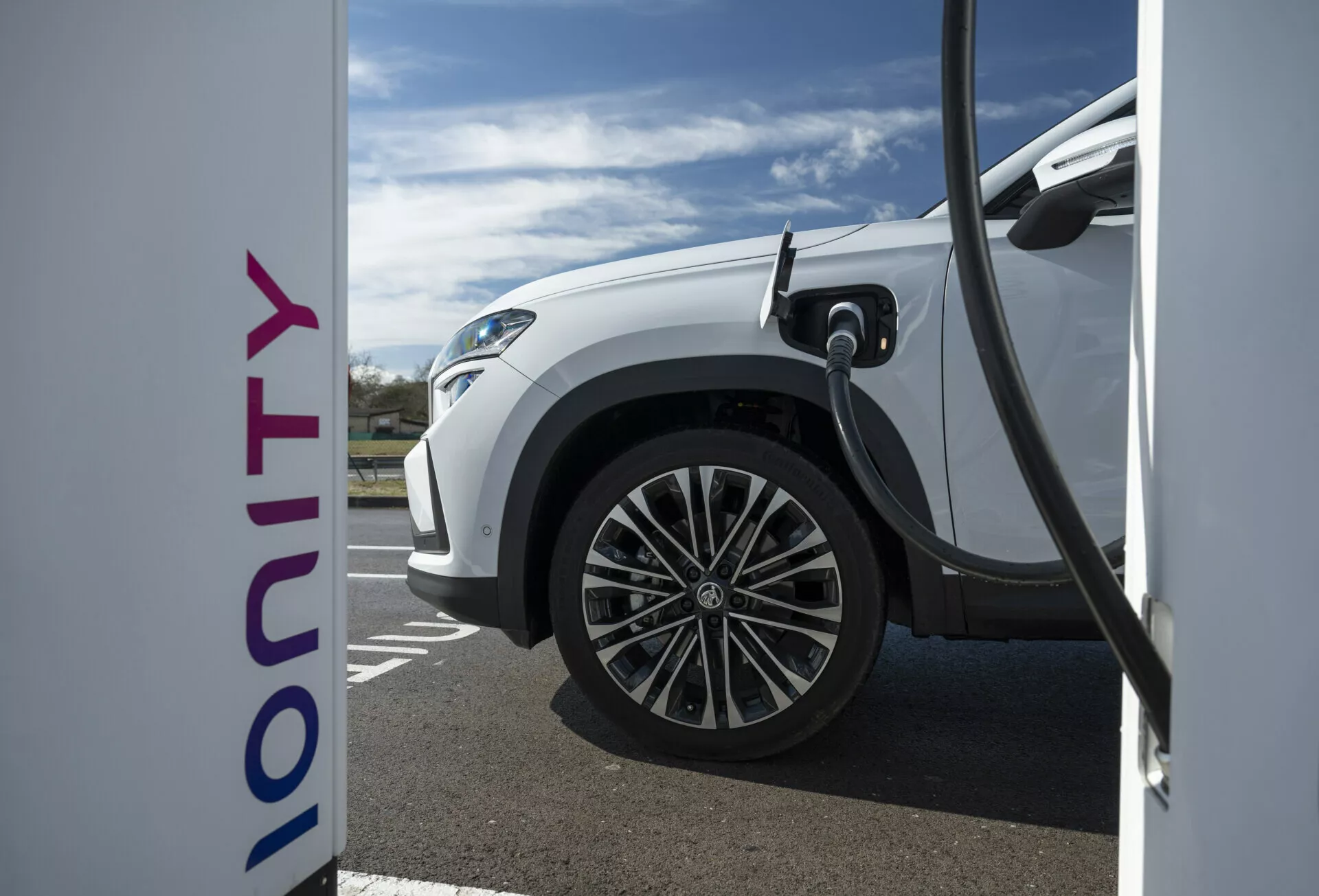 Vista laterale ravvicinata di una Škoda Kodiaq elettrica bianca 2024 in carica presso una stazione Ionity, evidenziando la tecnologia di ricarica rapida e il design moderno