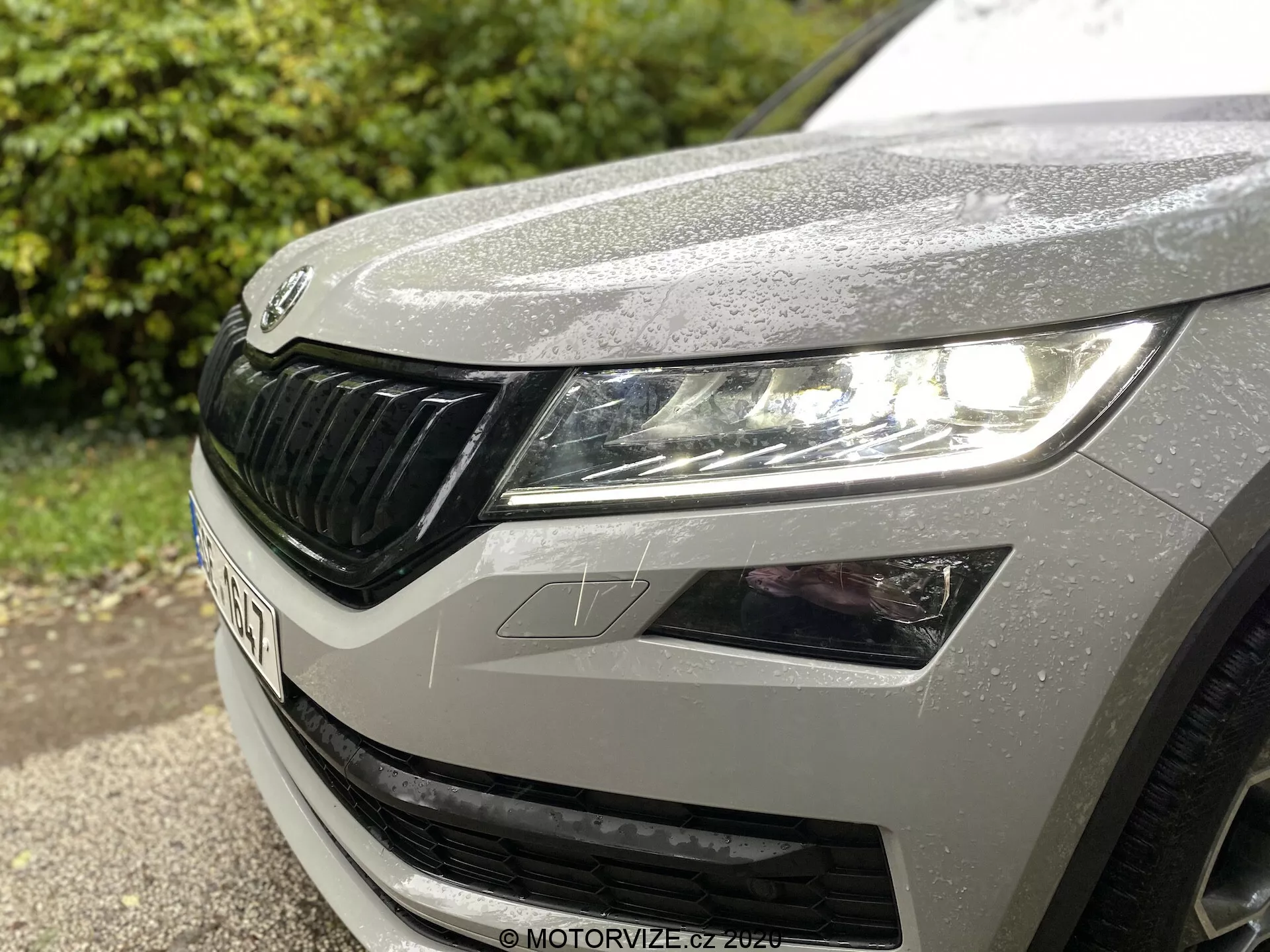 Vista ravvicinata del quarto anteriore sinistro di una Škoda Kodiaq 2017, che mostra il faro sinistro con design moderno a LED, parte del cofano con gocce di pioggia e la caratteristica griglia Škoda con elementi orizzontali.