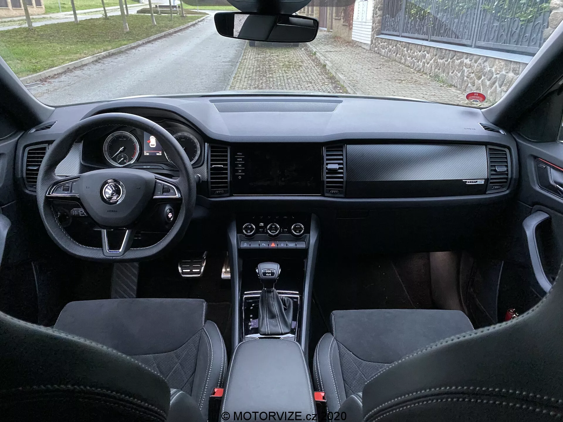 Vista interna della Skoda Kodiaq 2017 dallo spazio del sedile posteriore, che mostra cruscotto, volante con pulsanti multifunzione, quadro strumenti digitale, schermo infotainment ampio, controlli HVAC, selettore di cambio automatico, materiali in pelle premium e sedili sportivi con poggiatesta integrati.