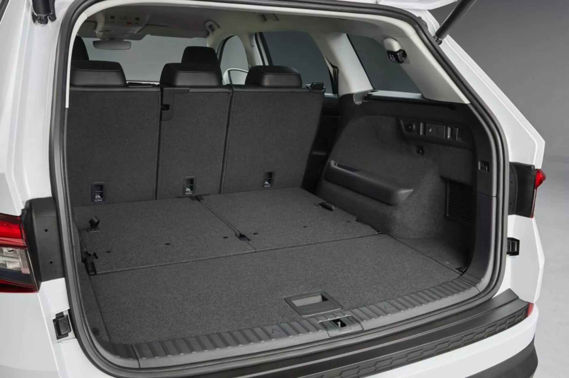 Vista dello spazio di carico posteriore Skoda Kodiaq 2017 con portellone aperto, mostrando una zona di carico moquette vuota, sedili posteriori abbattibili per spazio ampliato, bordo laterale in plastica con vano portaoggetti incassato, punti di ancoraggio e illuminazione interna, evidenziando soluzioni pratiche per lo stoccaggio e la gestione del carico.