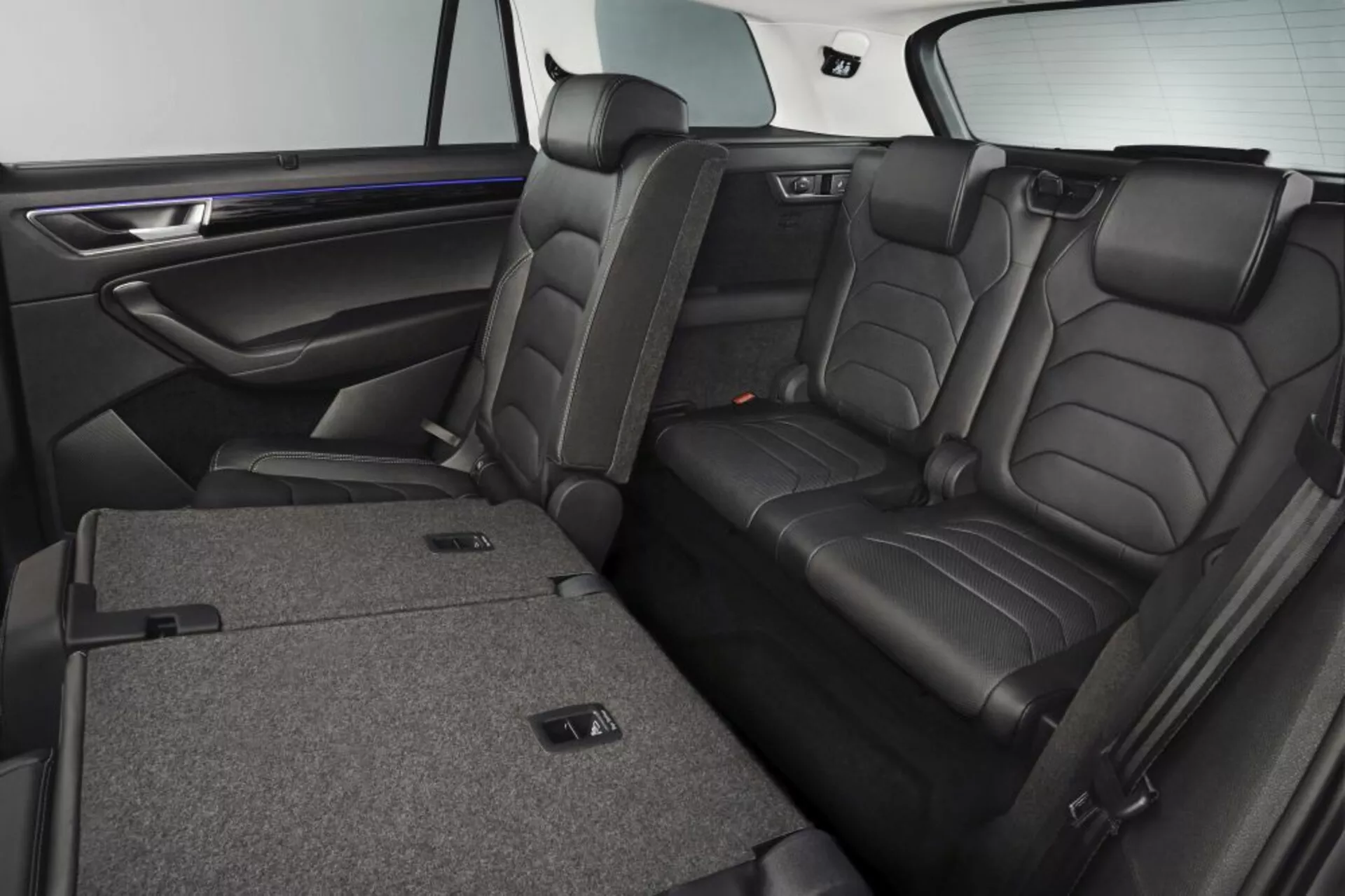 Interno della Skoda Kodiaq 2017 con sedili posteriori in pelle di lusso dotati di poggiatesta, funzione di ribaltamento diviso 60/40 per ampliare lo spazio di carico, bracciolo centrale con portabicchieri, e rivestimento delle porte effetto legno premium con illuminazione ambientale