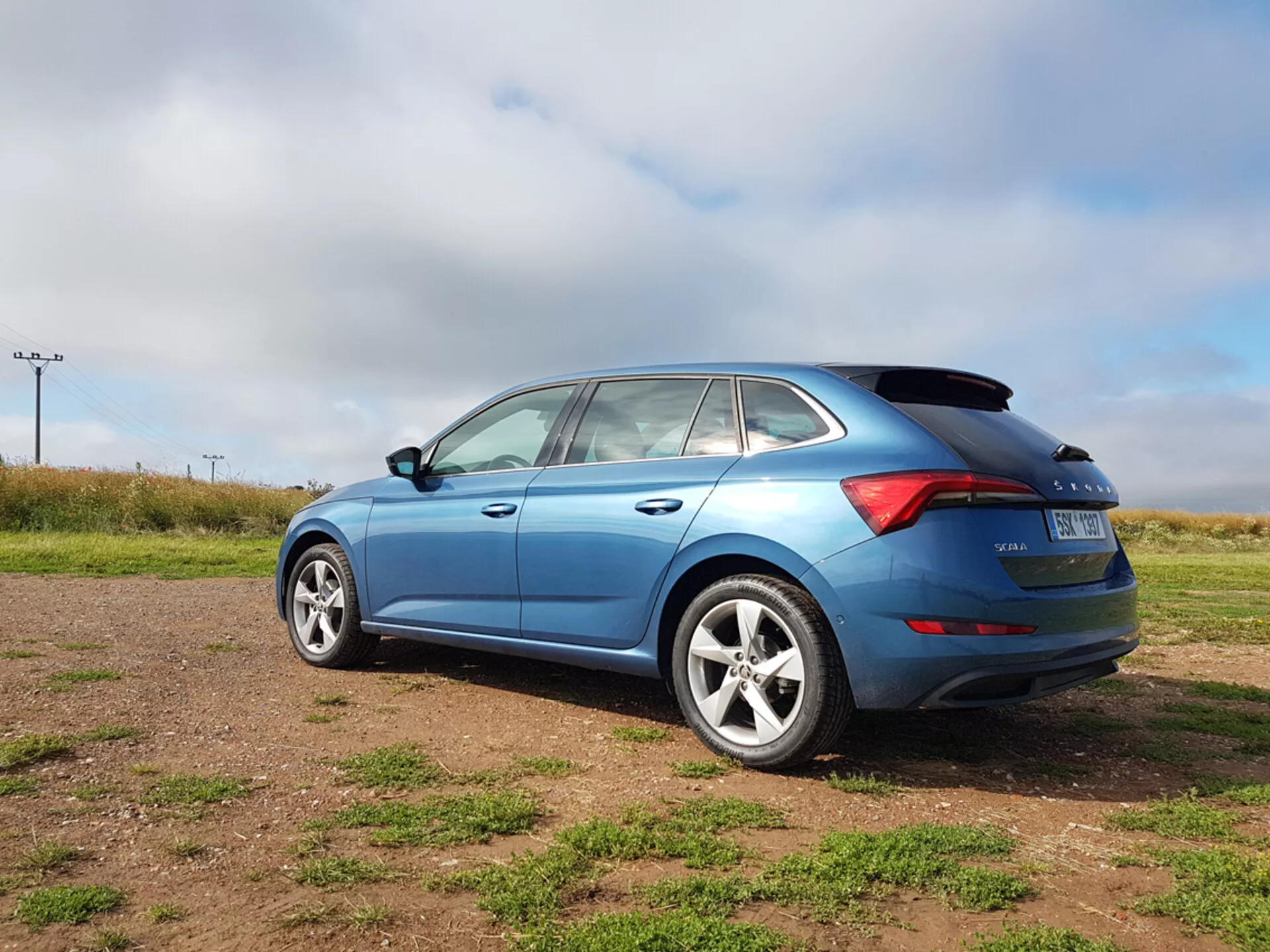Hatchback blu Skoda Scala 2019 che mostra gli elementi di design laterale e posteriore, inclusa la forma delle finestre, i fanali posteriori LED e le ruote in lega, fotografata da un angolo posteriore di tre quarti su un terreno erboso