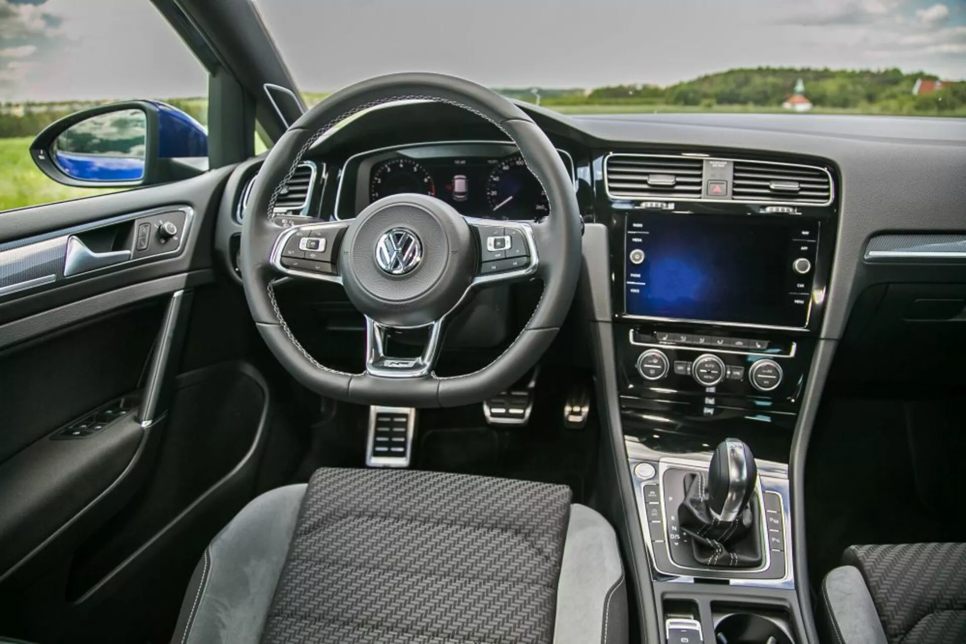 Vista interna di una Skoda Scala 2019 dalla prospettiva del passeggero anteriore che include volante multifunzione con logo Volkswagen, cruscotto digitale, touchscreen sulla console centrale e controllo automatico del clima