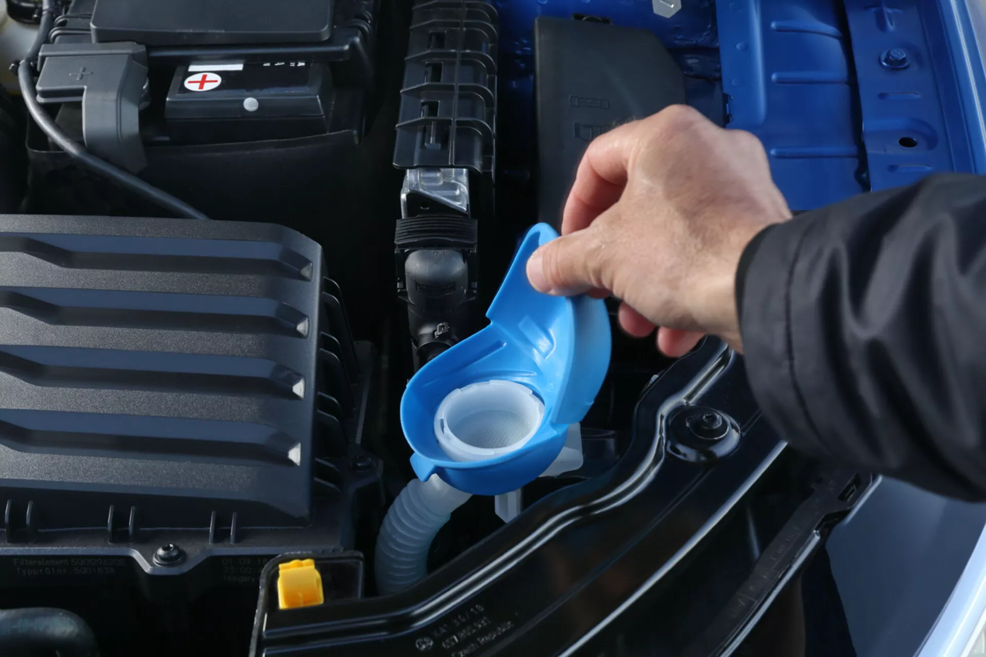 Primo piano di una persona che versa il liquido lavavetri nel vano motore di una Skoda Scala 2019, evidenziando il vano pulito e ben mantenuto con una batteria visibile e serbatoi di liquido