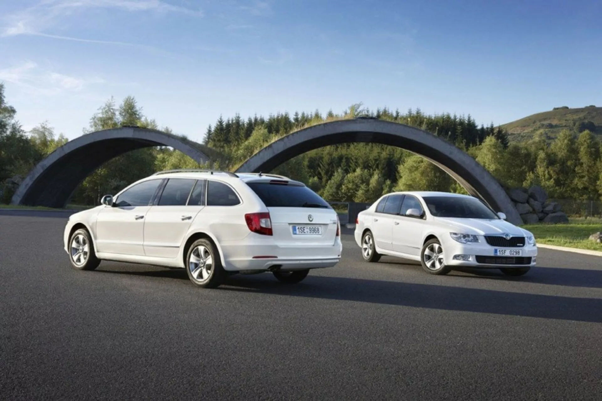 Skoda Superb station wagon del 2008 di giorno, mostrando angoli posteriori e frontali da tre quarti su una strada in asfalto contro vegetazione e un ponte curvo, con focus su elementi di design come fanali posteriori, griglia frontale e silhouette del veicolo.