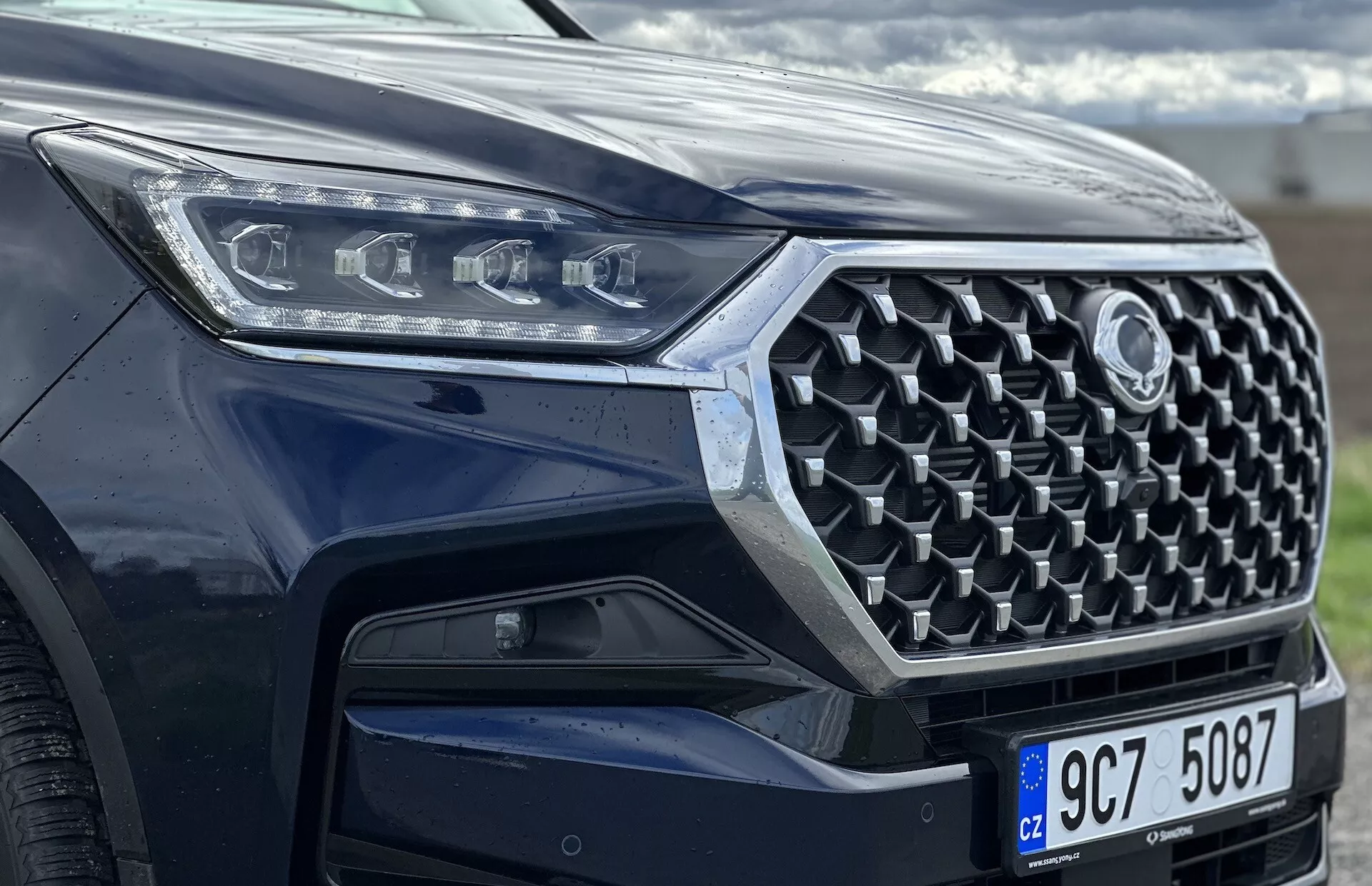 Vista frontale angolare di un SsangYong Rexton 2021 con focus sulla griglia, paraurti anteriore e design dei fari LED, evidenziando caratteristiche di sicurezza avanzate e tecnologia moderna con vernice metallica.