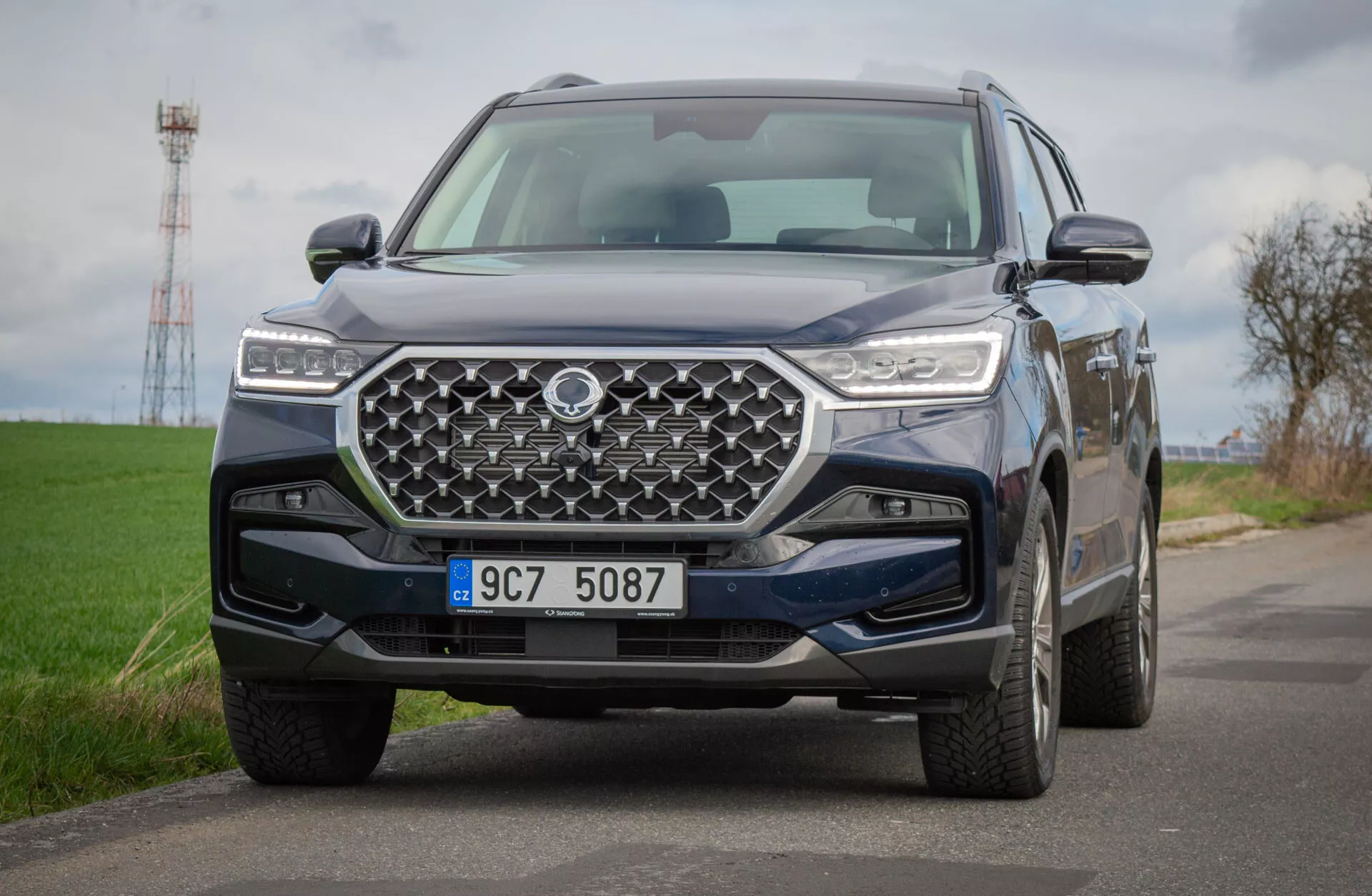 SUV SsangYong Rexton 2021 su strada di campagna, mostrando una vista dettagliata del suo design anteriore con griglia geometrica e fari LED, riflettendo tecnologia avanzata e capacità fuoristrada