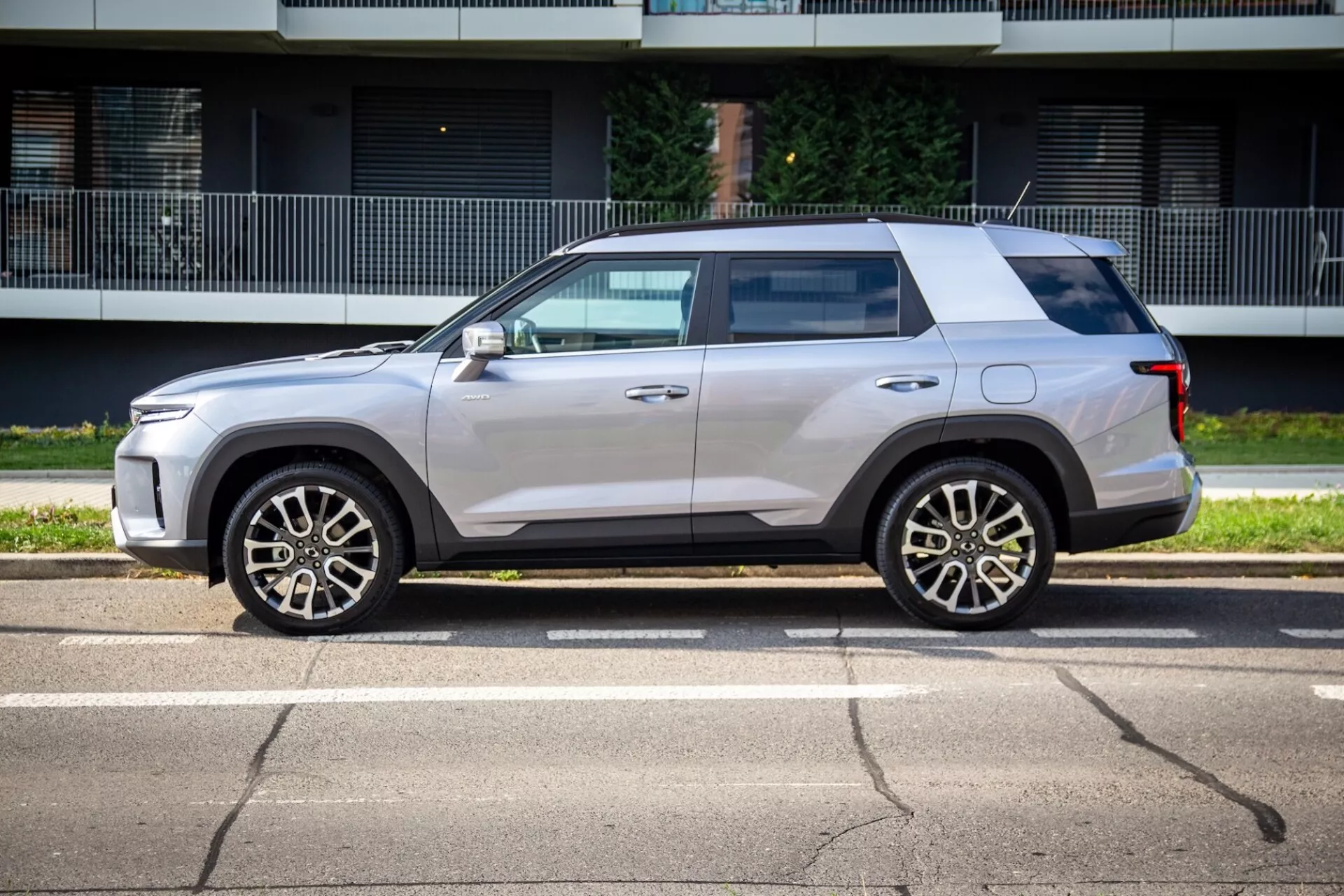 Vista laterale del SsangYong Torres 2023 che mostra il suo design squadrato ma aerodinamico, linea di cintura alta, tetto piatto e vernice metallica chiara con ruote in lega a cinque razze, specchietti laterali color carrozzeria con indicatori di direzione integrati, leggera tonalità dei vetri, maniglie delle porte a filo e rivestimento nero in una strada soleggiata
