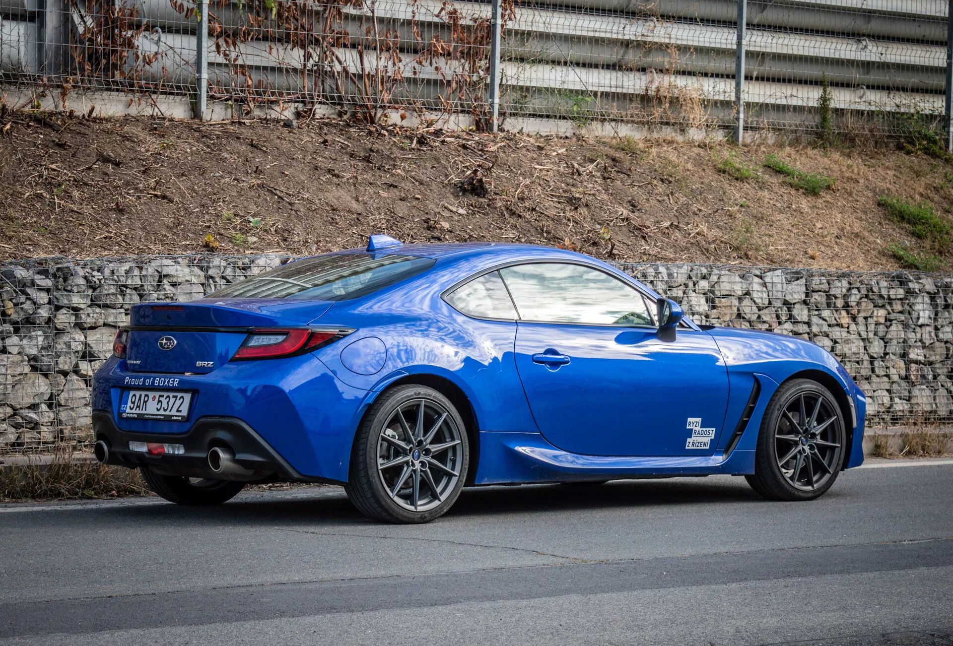 Coupé sportiva Subaru BRZ 2023 di colore blu brillante con design aerodinamico parcheggiata su una strada, che mostra l'arco della ruota posteriore, luci posteriori, curvatura del finestrino posteriore fino al coperchio del bagagliaio, linee scolpite, tetto inclinato, ruote in lega a più razze, freni ad alte prestazioni, spoiler posteriore basso, doppi tubi di scarico nel diffusore posteriore, specchietti laterali color carrozzeria e un cofano lungo e sportivo.