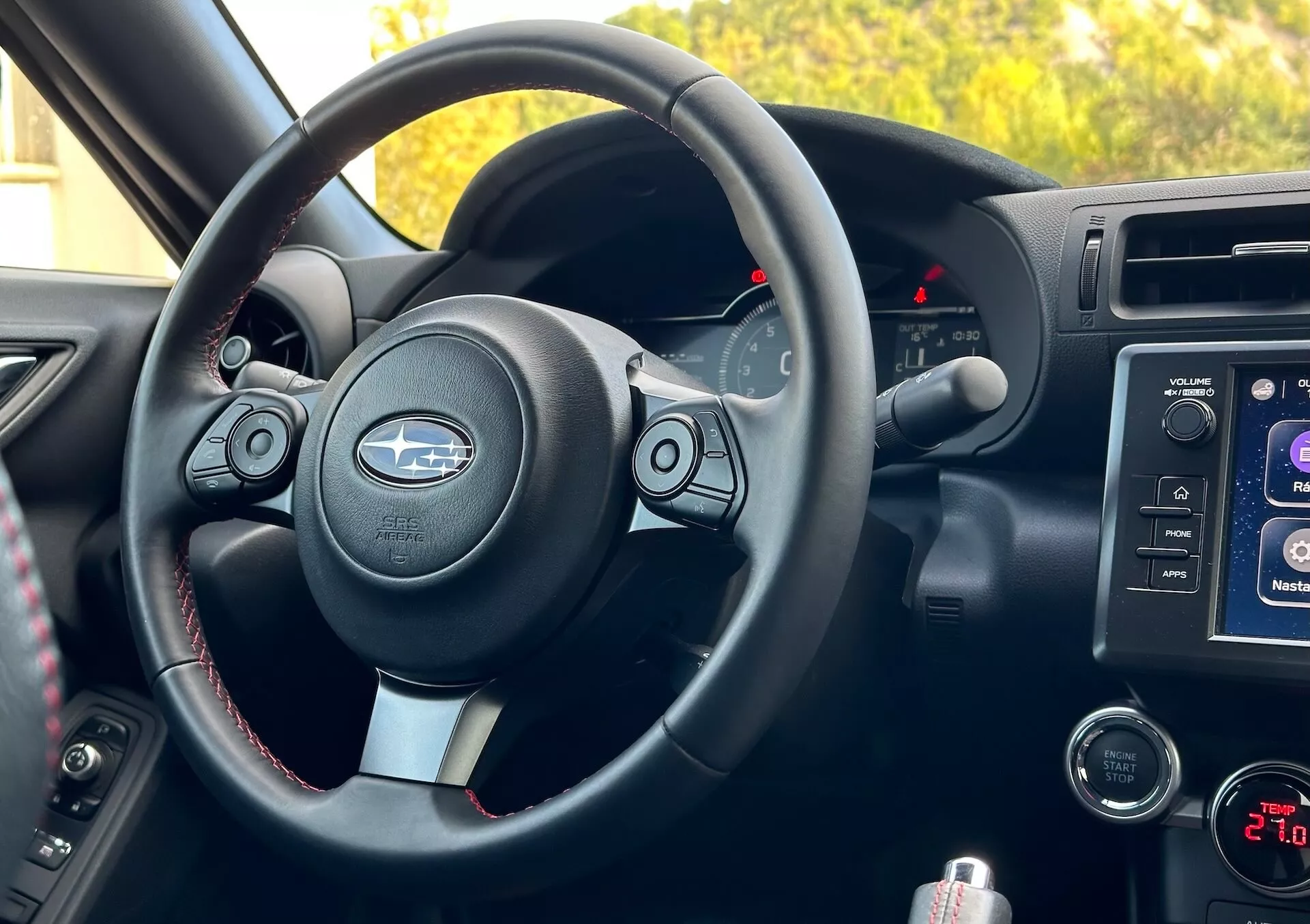 Vista interna della Subaru BRZ 2023 dalla prospettiva del passeggero che mostra il volante con accenti metallici e logo Subaru, pulsanti di controllo, cuciture a contrasto, cluster strumenti con indicatori retroilluminati, sistema di infotainment nella consolle centrale, comandi audio e clima, e vano portaoggetti.