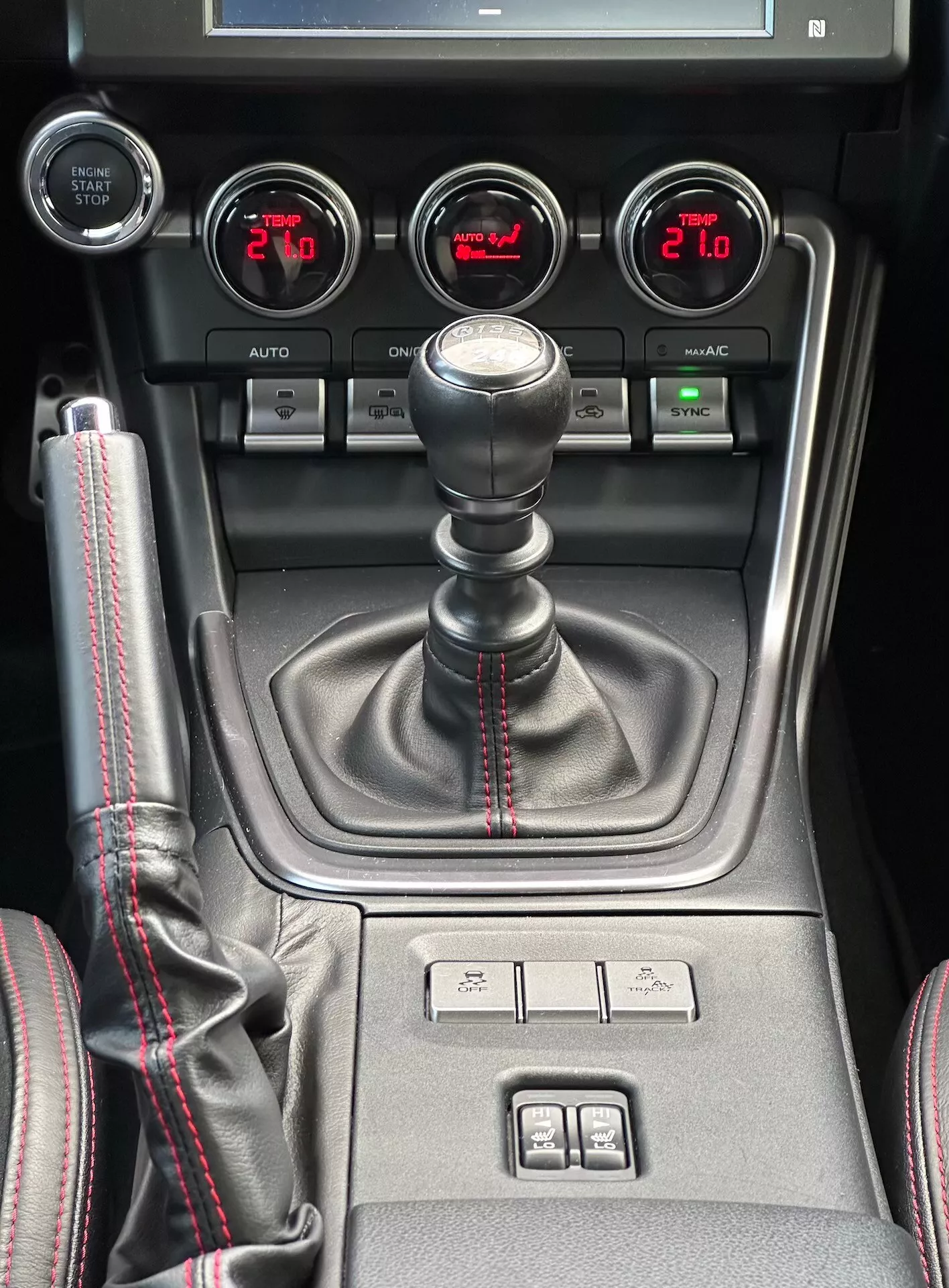 Console centrale Subaru BRZ 2023 con leva del cambio manuale con cuciture rosse sportive, manometri ausiliari per pressione del turbo, tensione della batteria, temperatura dell'olio e controllo del clima a doppia zona in vista dettagliata dell'interno