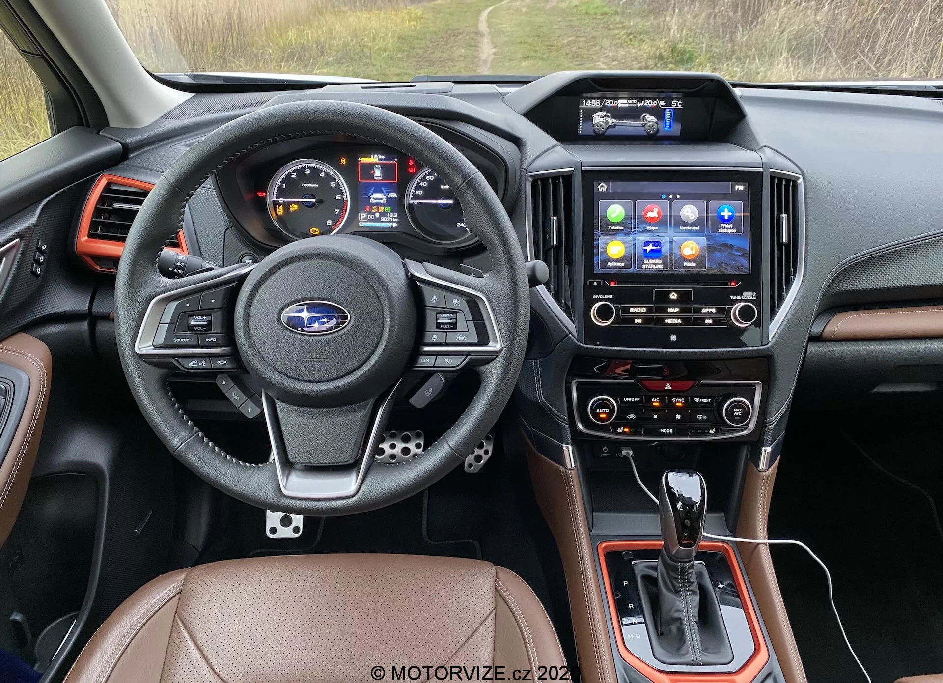 Scatto dell'interno dal sedile del conducente di un Subaru Forester 2020, focalizzato sul cruscotto, volante, sistema di infotainment e console centrale. Il volante in pelle a tre razze comprende comandi multifunzione per audio, telefono, comandi vocali e controllo della velocità di crociera, con il logo Subaru al centro. Il pannello strumenti include un display digitale e indicatori analogici per velocità e giri/min. La console centrale ospita la leva del cambio dell'automatico, controlli aggiuntivi e un possibile selettore della modalità di guida. Il touchscreen dell’infotainment con varie icone di applicazioni offre navigazione, media, connettività telefonica e configurazioni del veicolo. Sotto, i controlli climatici suggeriscono impostazioni a doppia zona per conducente e passeggero anteriore. Le finiture interne includono sedili in pelle o similpelle, componenti in plastica nera e accenti metallici. Le bocchette dell'aria fiancheggiano il sistema di infotainment e i bordi del cruscotto. Questa immagine si classifica in interni di automobili, tecnologia automobilistica, cruscotti, sistemi di infotainment e controlli climatici.