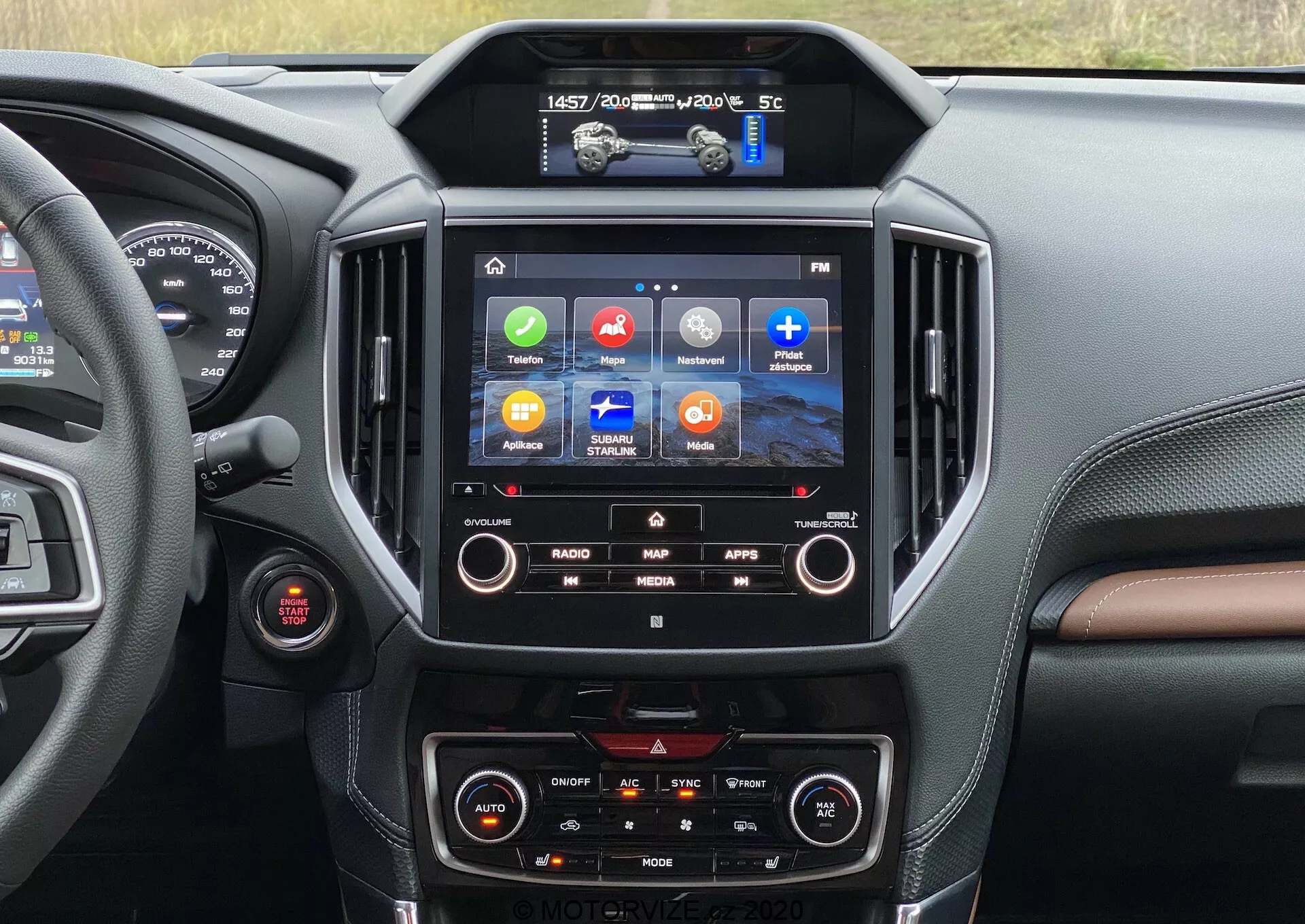 Vista interna di una Subaru Forester 2020 focalizzata sulla consolle centrale e sul sistema di infotainment. Il display touchscreen mostra icone colorate per Radio, Mappa, App e Media, indicando funzionalità come navigazione GPS, integrazione di applicazioni e riproduzione multimediale. Sotto di esso, sono visibili i comandi del clima a doppia zona. Un'occhiata all'area del conducente rivela un quadrante rosso, probabilmente il pulsante di avvio/arresto del motore. Il design degli interni presenta materiali simili alla pelle scura e marrone con cuciture, offrendo una sensazione di lusso.