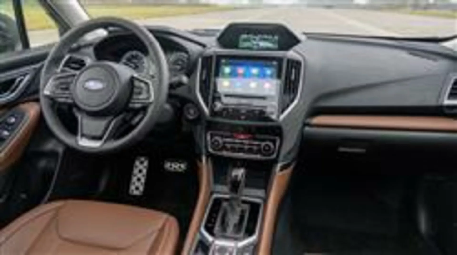 Interni della Subaru Forester 2015 con cruscotto, volante multifunzione, sistema di infotainment touch screen, selettore di trasmissione automatica e accenti di materiali di lusso visti dal lato passeggero