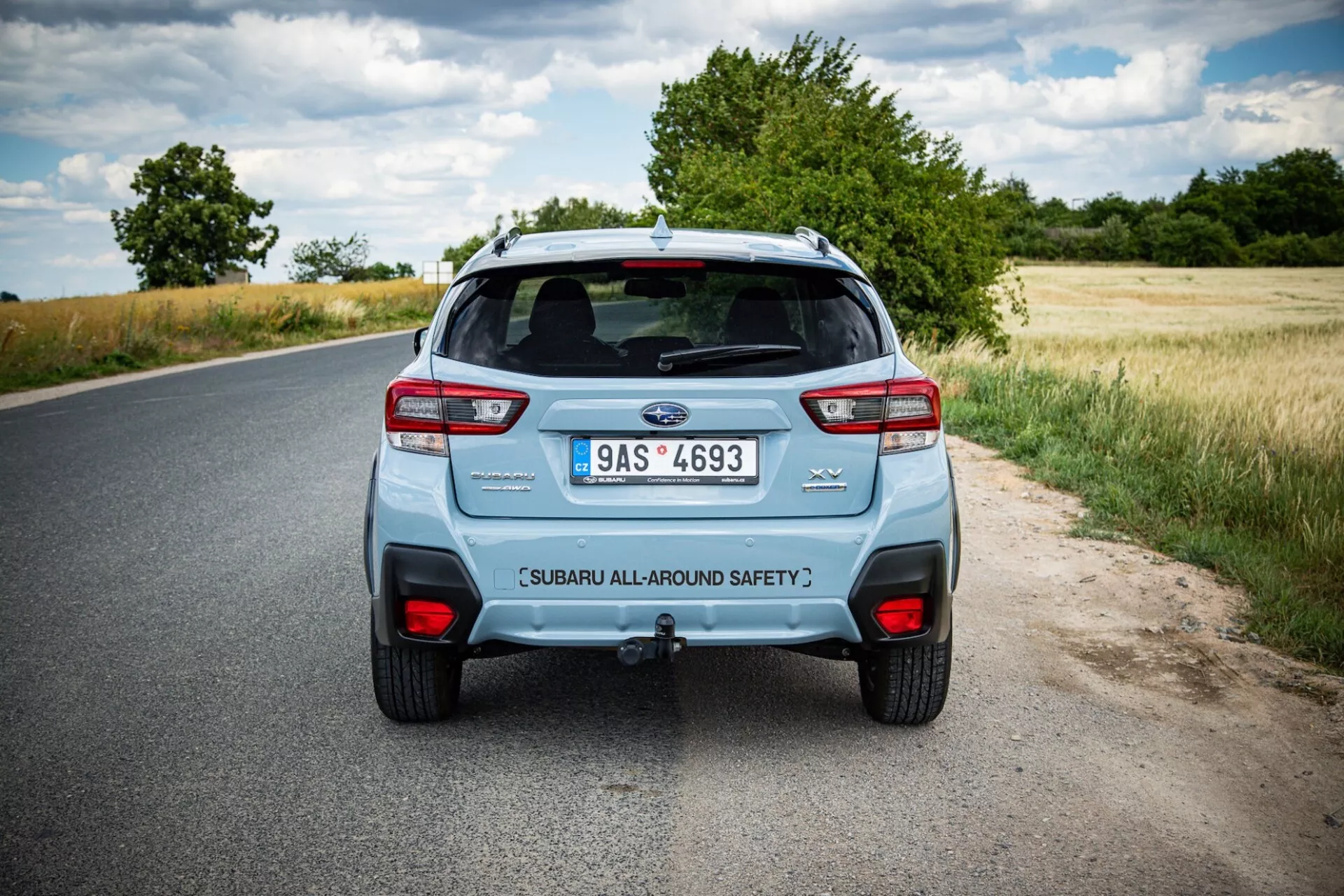 Vista posteriore di una Subaru XV 2021 su una strada rurale, mostrando le distintive luci posteriori dell'auto, sistema di scarico doppio e portellone con etichetta di sicurezza sotto un cielo parzialmente nuvoloso
