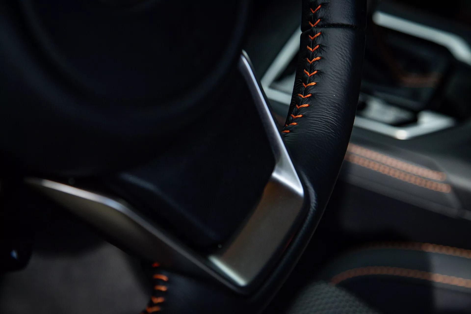 Vista dettagliata dell'interno della Subaru XV 2021 con focus sul lato guidatore con parte del volante in colore nero e cuciture arancioni o rosse, accanto a un pannello porta dettagliato con pelle o similpelle nera e accenti in trim metallico