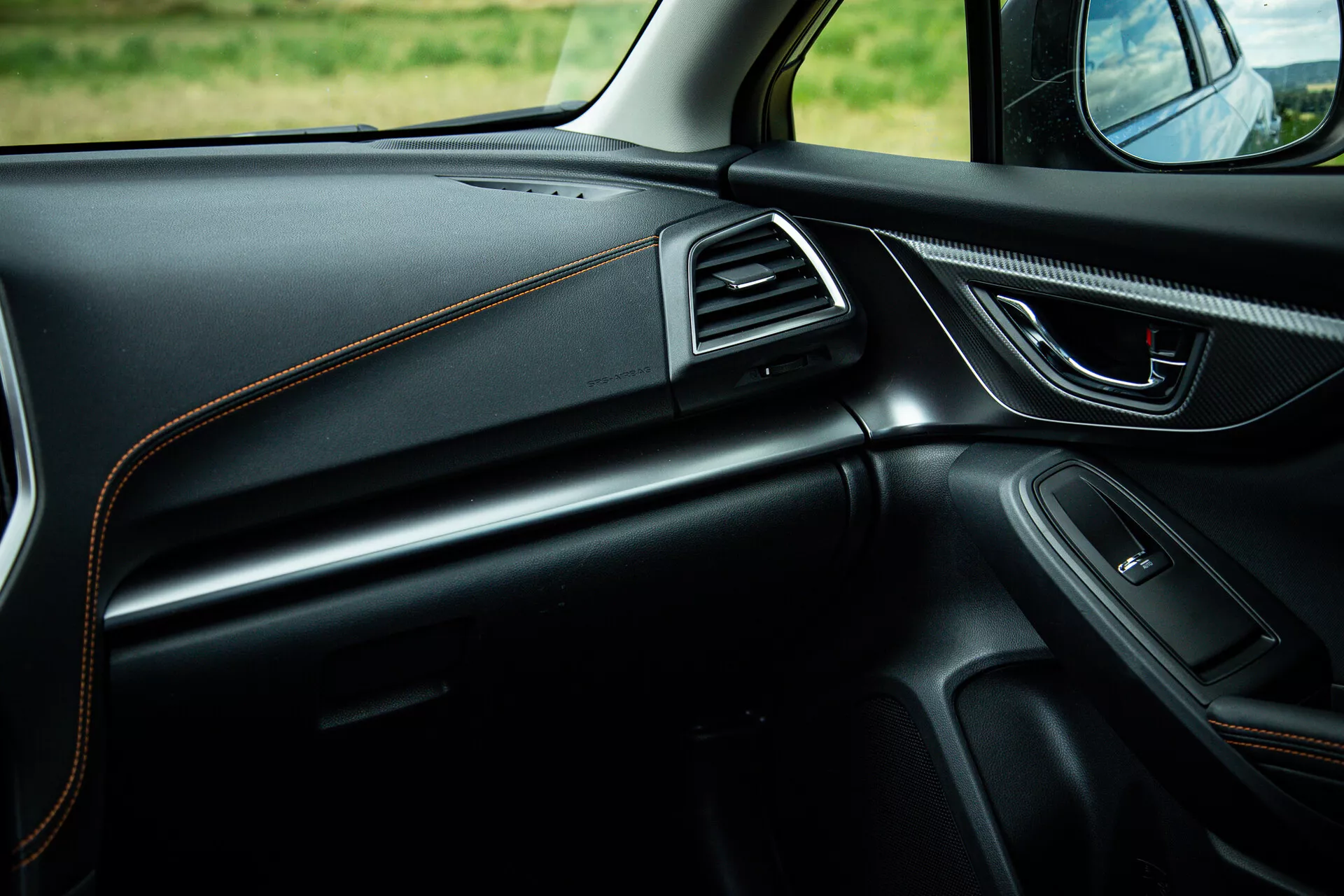 Vista interna della Subaru XV 2021 con focus sul lato passeggero che mostra design elegante della plancia con cuciture a contrasto, maniglia della porta ergonomica con controlli elettrici, altoparlante integrato, bocchette dell'aria con rifiniture in cromo e illuminazione ambientale