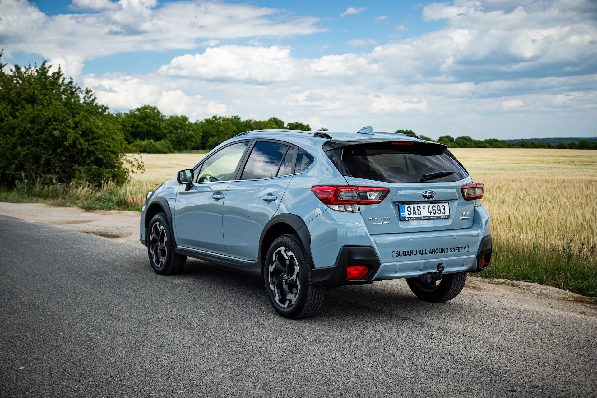 Subaru XV compact SUV blu chiaro 2021 fotografato da un angolo posteriore a tre quarti che evidenzia il lato destro, posizione dinamica su strada asfaltata con vista chiara dello spoiler posteriore, cerchi in lega, fari posteriori LED, badge del modello, singolo terminale di scarico e potenziali caratteristiche tecnologiche