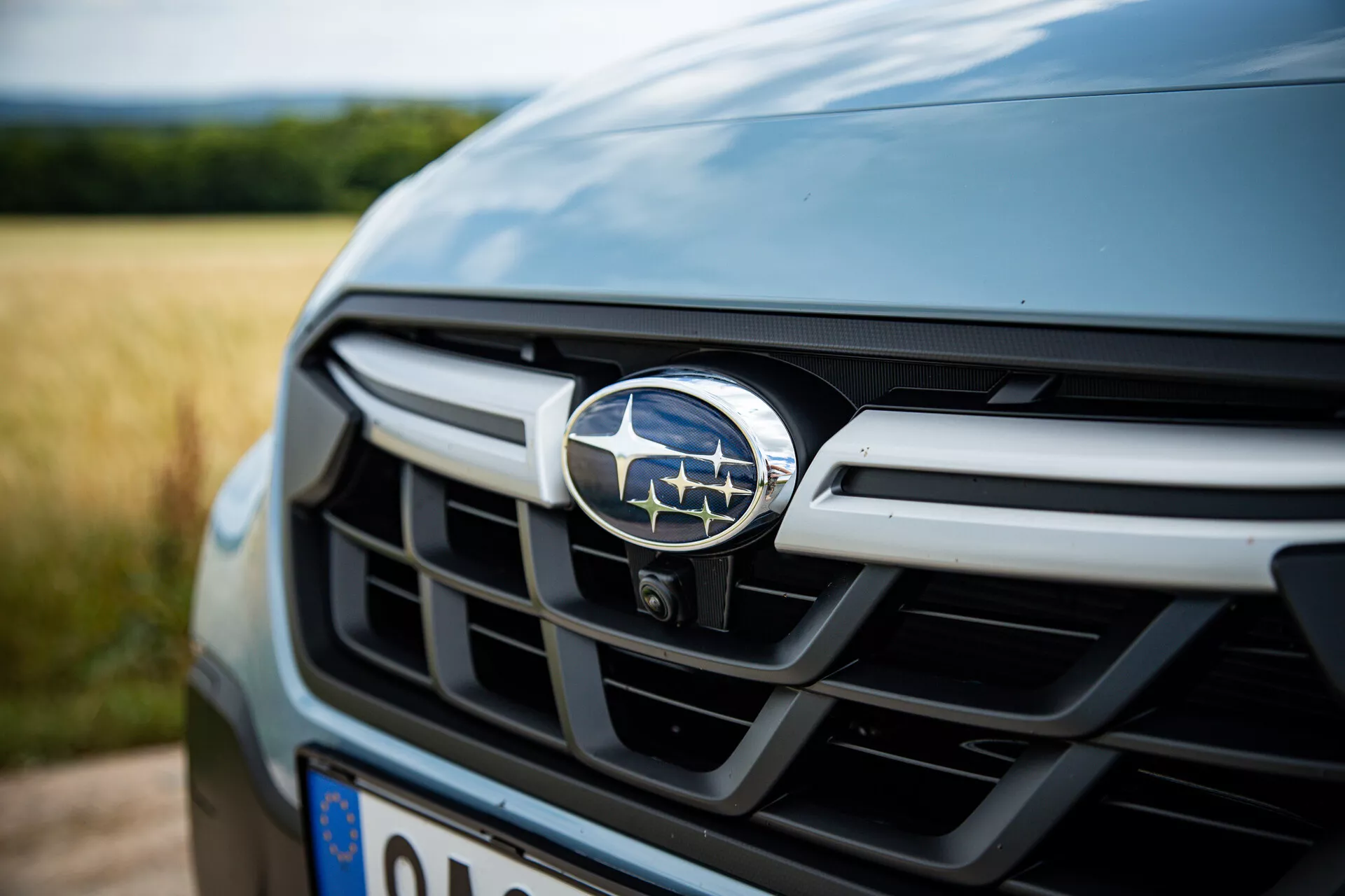 Vista ravvicinata della griglia frontale e dell'emblema della Subaru XV 2021, che mostra le sue lamelle orizzontali metalliche, in una tonalità scura, con una profondità di campo ridotta che mette a fuoco il distintivo e suggerisce caratteristiche automobilistiche di lusso.