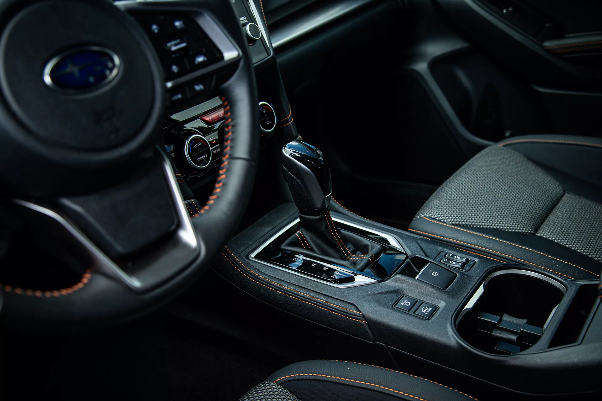 Vista ravvicinata dell'interno di una Subaru XV 2021 con focus sulla console centrale e sull'area del cambio dal lato passeggero, mostrando pulsanti multifunzione sul volante, selettore di trasmissione automatico con guaina in pelle e accenti metallici, e caratteristiche di design interno di fascia alta come il freno di parcheggio elettronico e il sistema di controllo del clima.