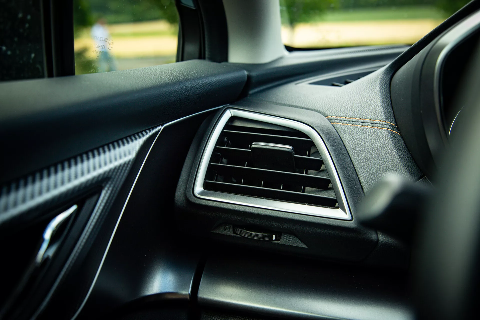 Dettaglio interno Subaru XV 2021 che mostra il cruscotto lato passeggero con bocchetta d'aria accentata in cromo, rivestimento in pelle nera di qualità con cuciture visibili e materiali morbidi al tatto, fotografato da un angolo di 45 gradi evidenziando elementi di design moderno alla luce naturale del giorno