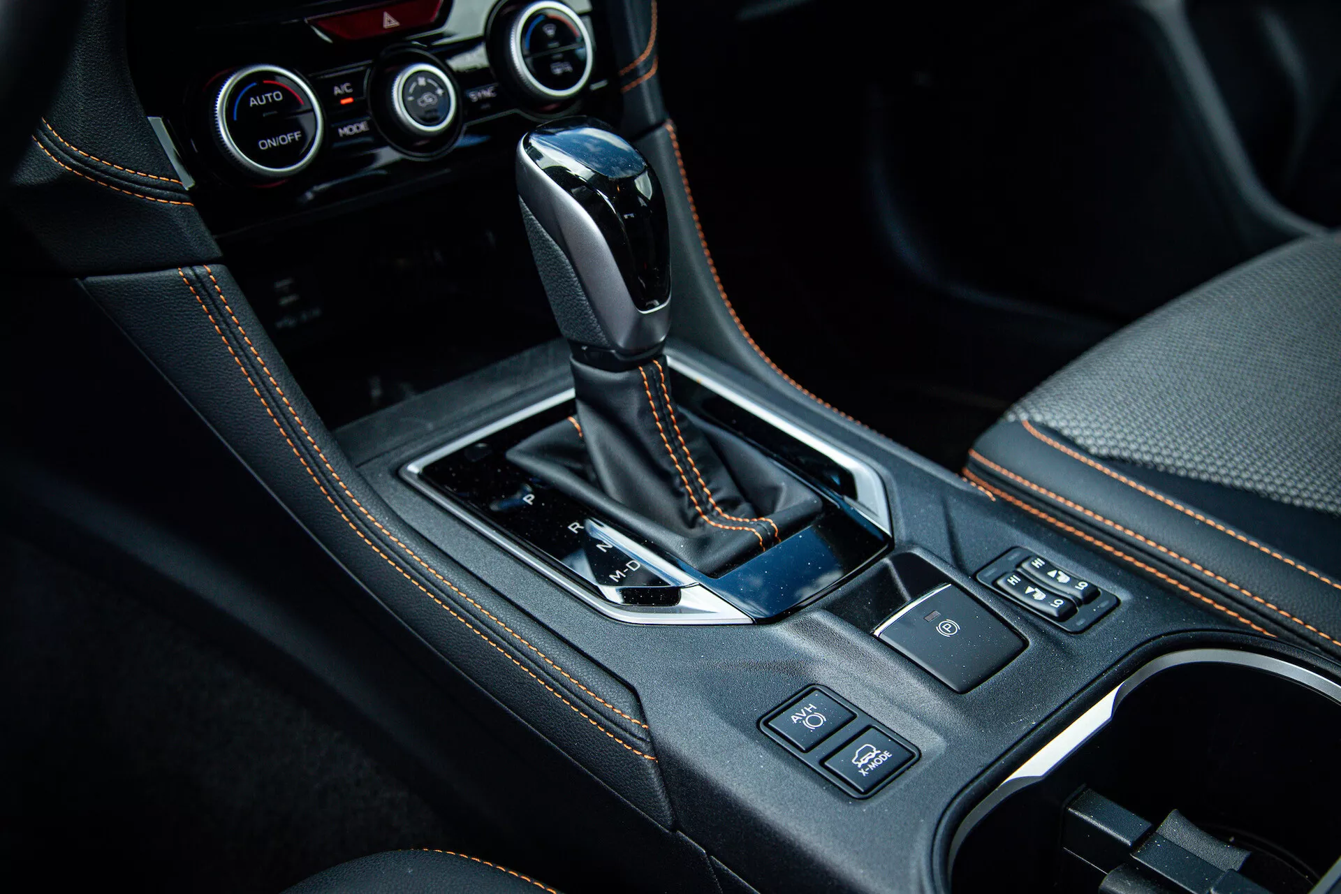 Console centrale Subaru XV 2021 con leva del cambio automatico rivestita in pelle, inserti in nero lucido, dettagli cromati, portabicchieri, pulsanti di controllo e sistema di controllo climatico avanzato visibile in foto degli interni di alta qualità