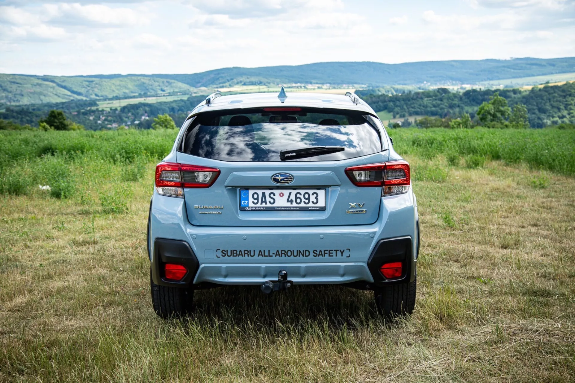 Angolo posteriore del Subaru XV 2021 all'aperto in un campo con colline sullo sfondo, evidenziando le caratteristiche di sicurezza e gli elementi di design moderno SUV come lo spoiler posteriore e i fari posteriori audaci
