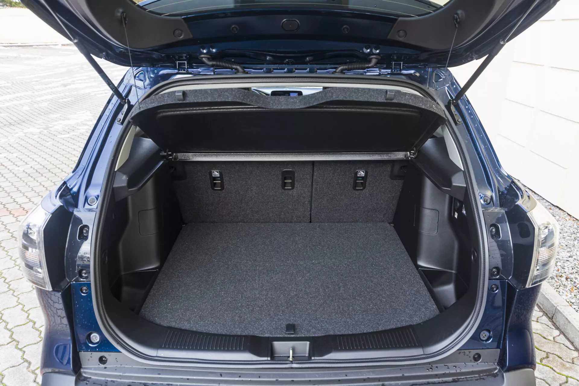 Vista dello spazio bagagliaio posteriore di Suzuki S-Cross 2022 con coperchio aperto che mostra un'area tappetata vuota, scomparti laterali e sedili posteriori abbattuti
