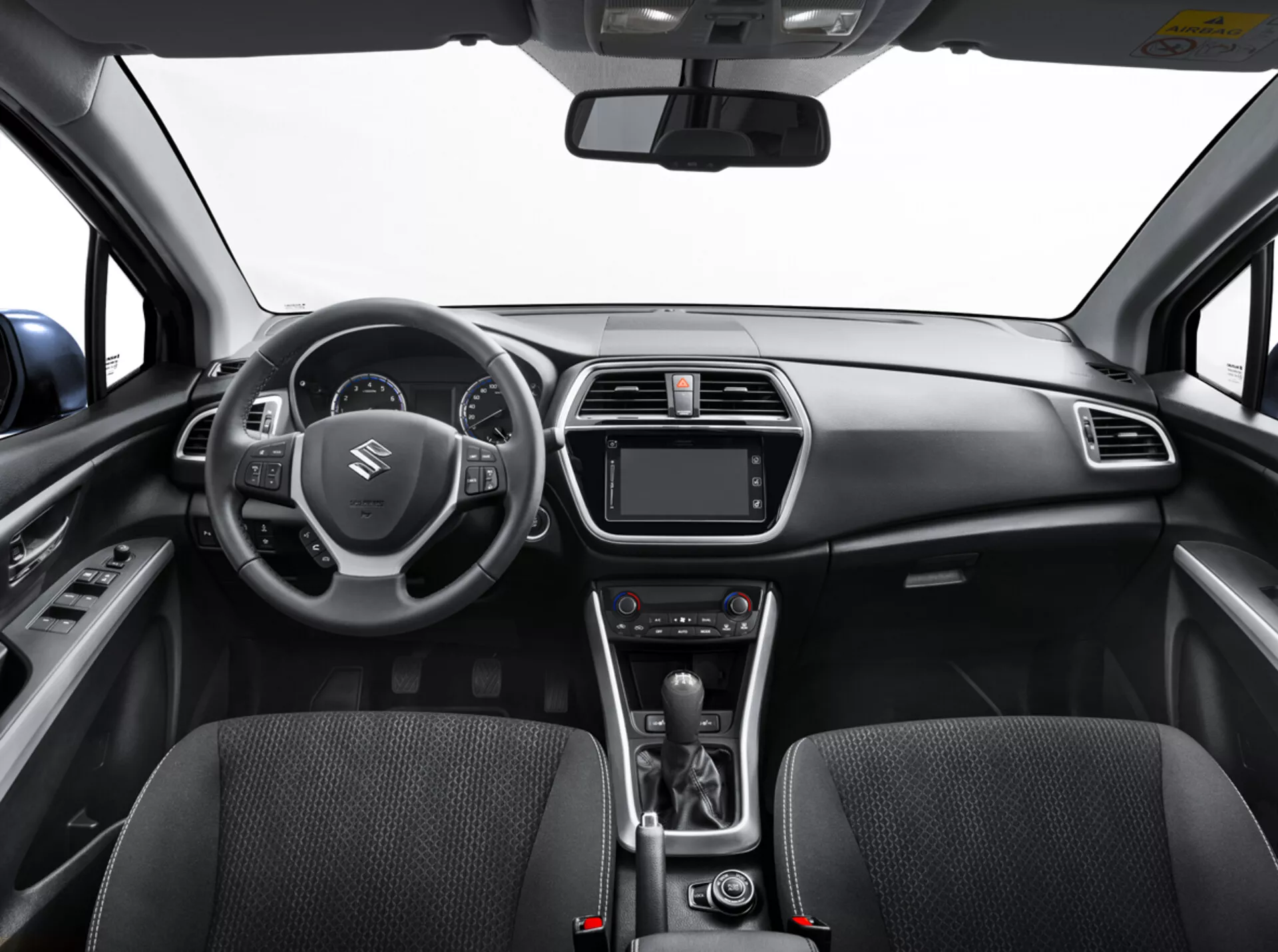 Vista interna della Suzuki S-Cross 2022 dal sedile posteriore che mostra il cruscotto, il volante con controlli, il cluster strumenti digitale, il sistema di infotainment, i controlli del clima, la leva del cambio automatico e i sedili anteriori dettagliati con texture in tessuto